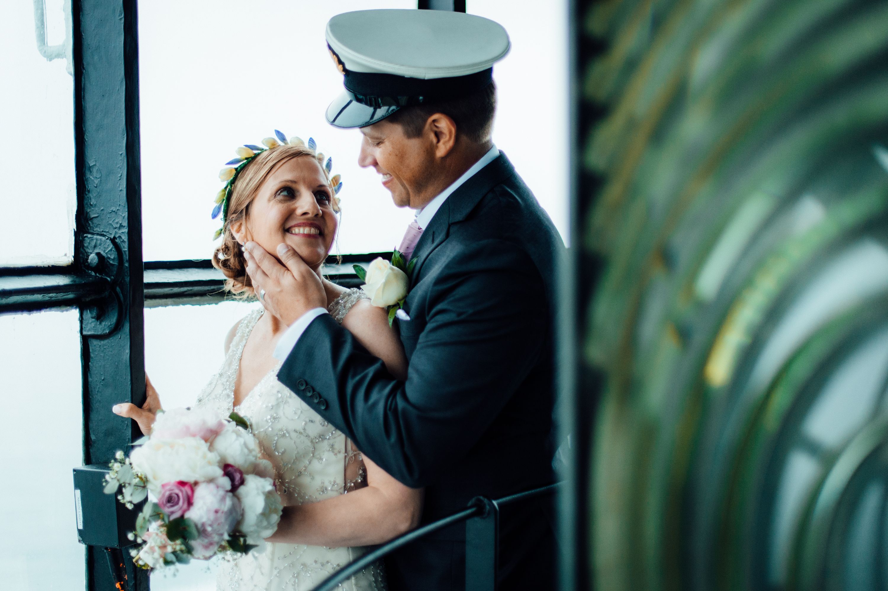 Groom wears a nautical sailor’s outfit while holding his bride’s face romantically