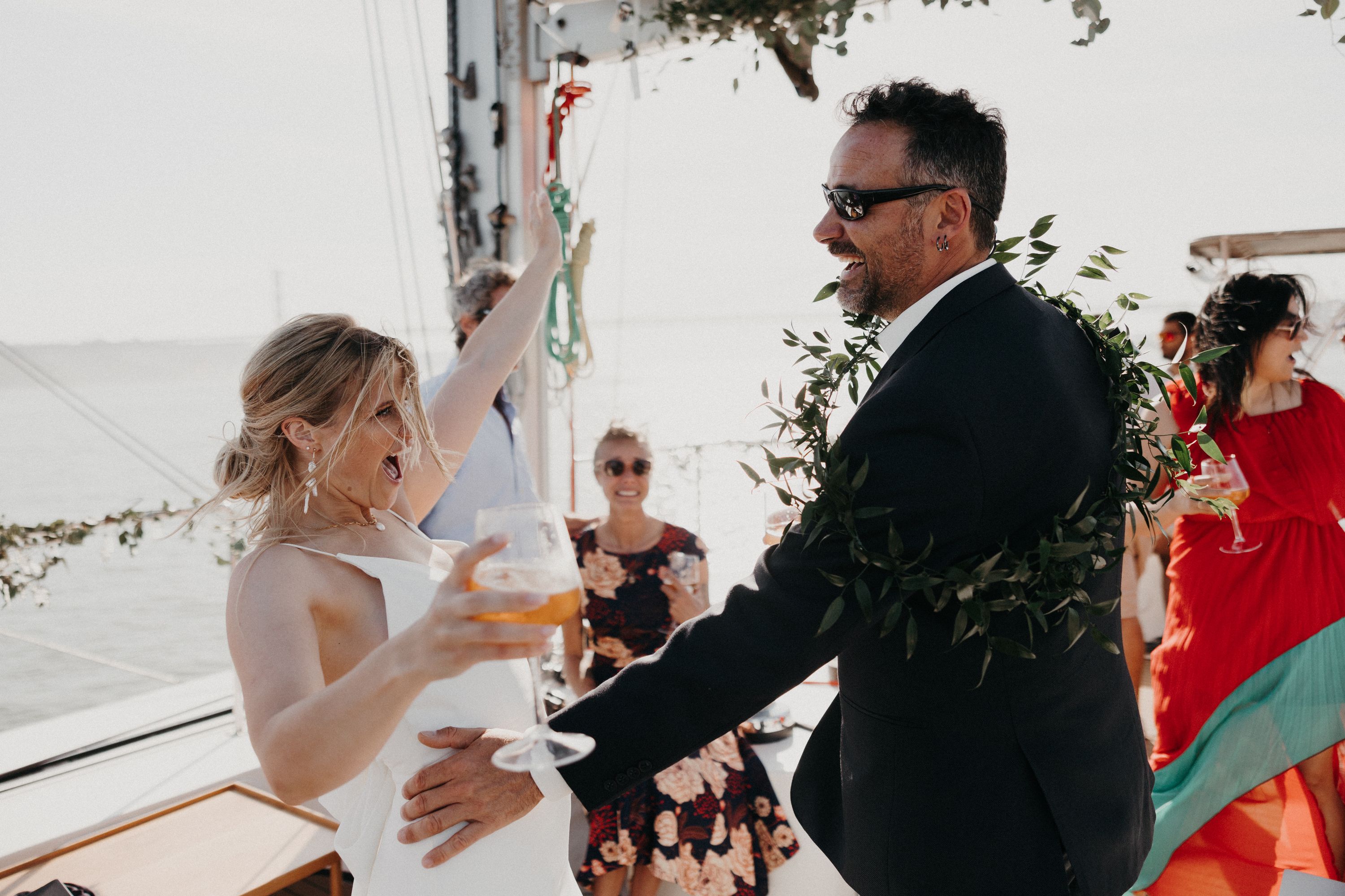 Bride holds a glass of wine while her groom touches her on the side in a sailboat destination wedding in Portugal