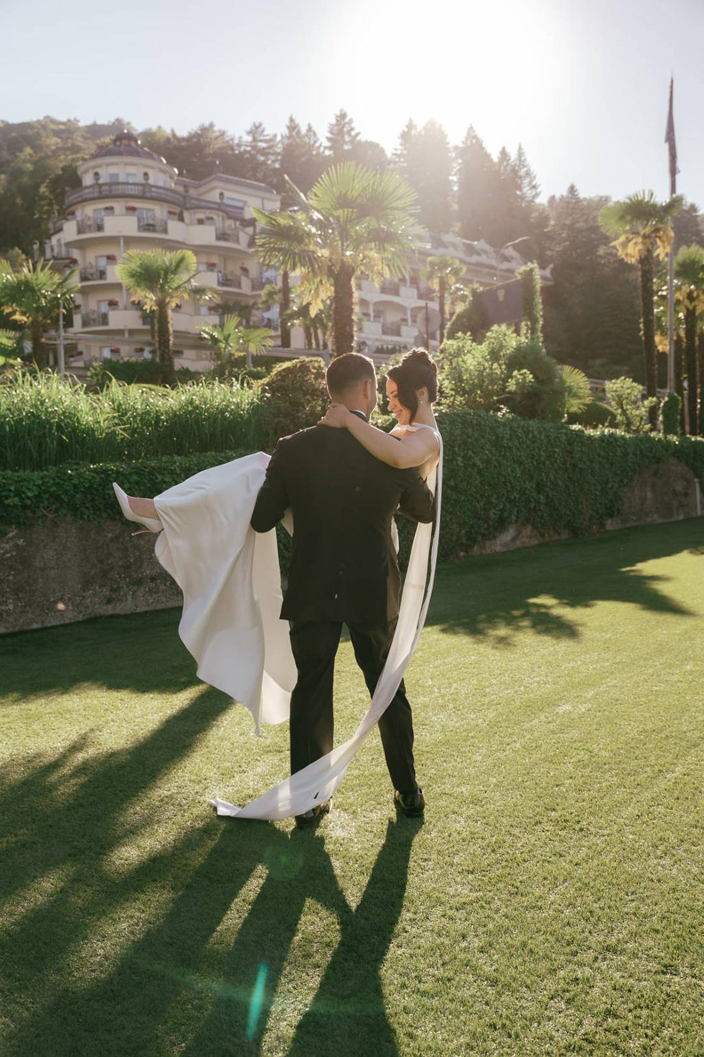 Groom carrying the bride across a manicured lawn during an intimate wedding in Italy celebration