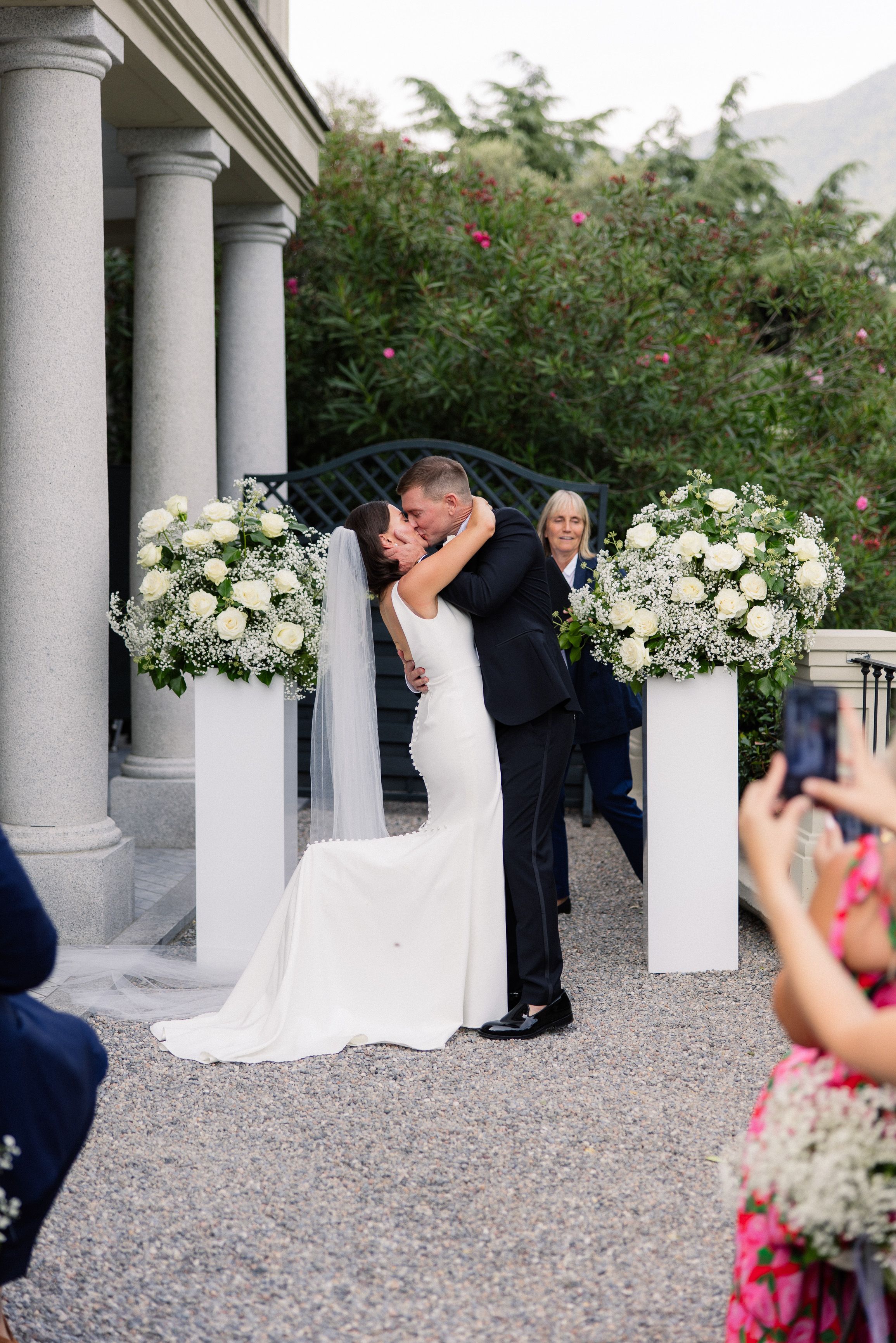 Newlyweds sharing their first kiss beneath white floral displays at an intimate wedding in Italy