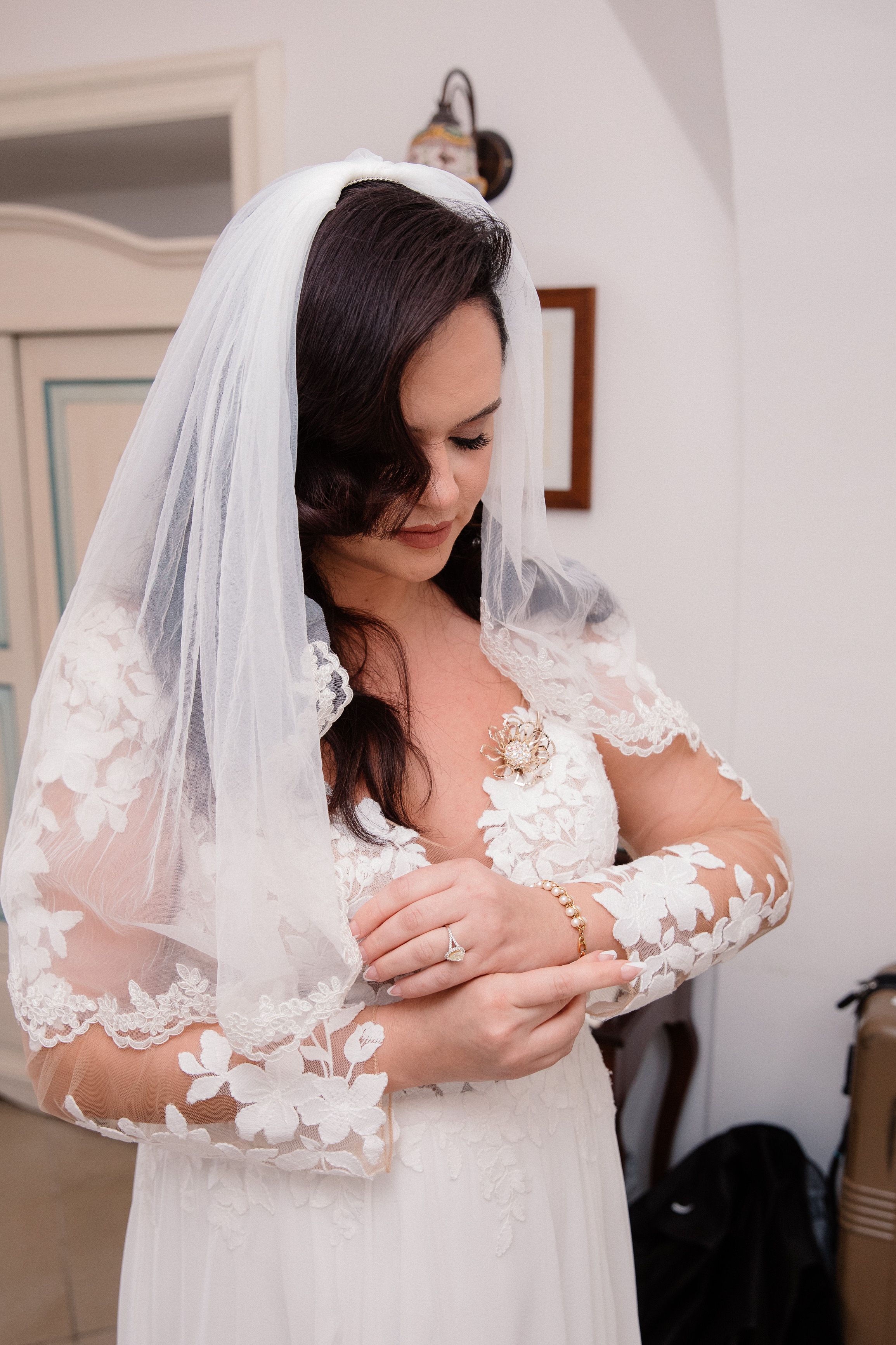 Bride adjusting her bracelet while getting ready for an intimate wedding in Italy, wearing a lace gown and elegant veil.