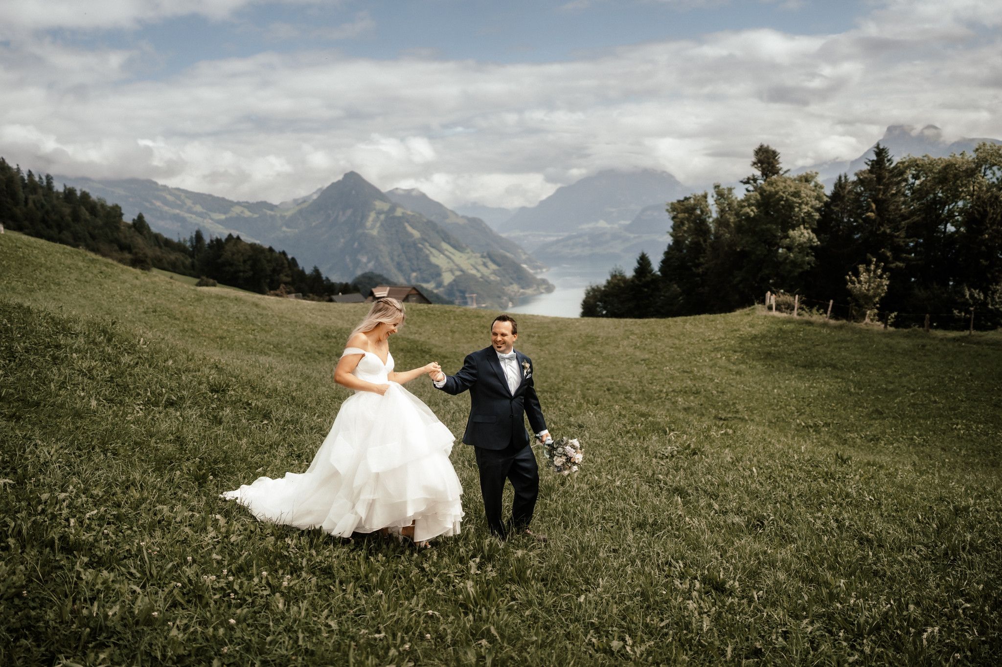 a bride and groom in the meadows of Switzerland with mountains and a river in the background