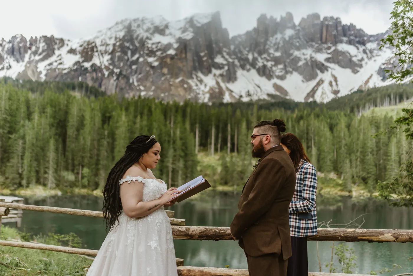 Bride recites vows in front of her groom during their elopement in Italy with Lake Carezza and alpine scene as backdrop