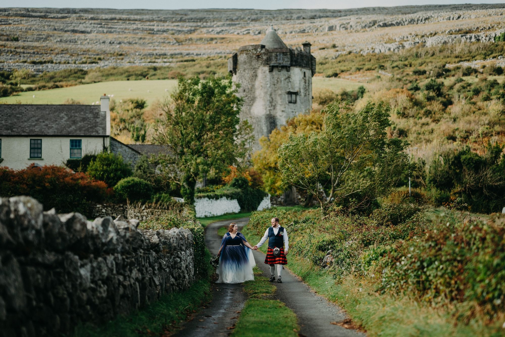 Newlyweds walk a narrow path amidst the autumn nature of Clare with a castle in the background when they eloped in Ireland