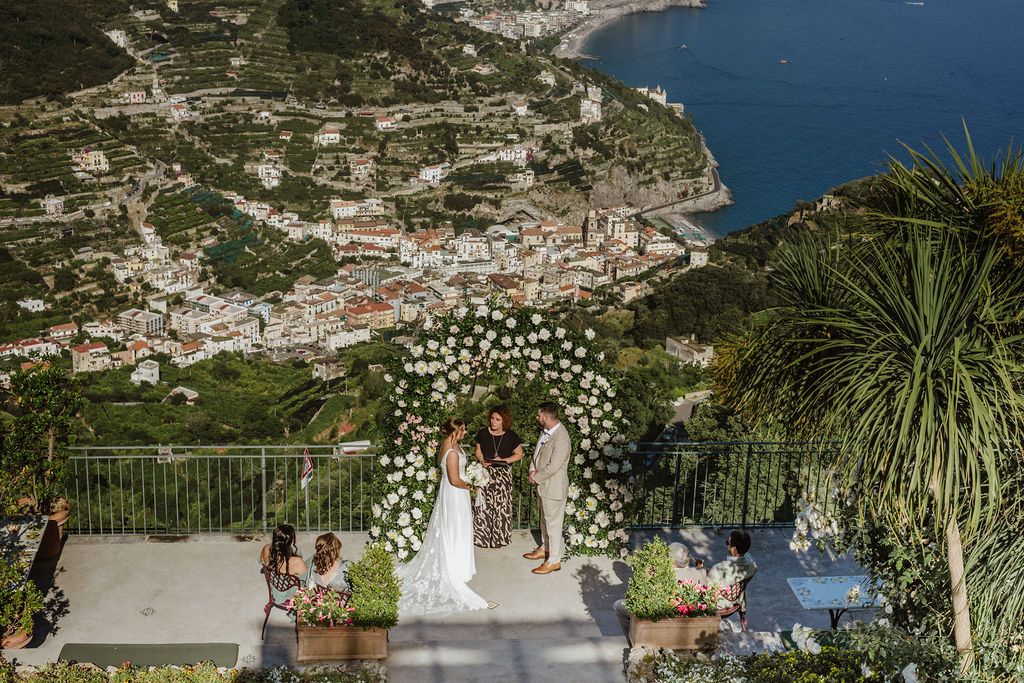 Bride and groom having a ceremony at the terrace of a hotel during their elopement in Italy, with mountain and sea views