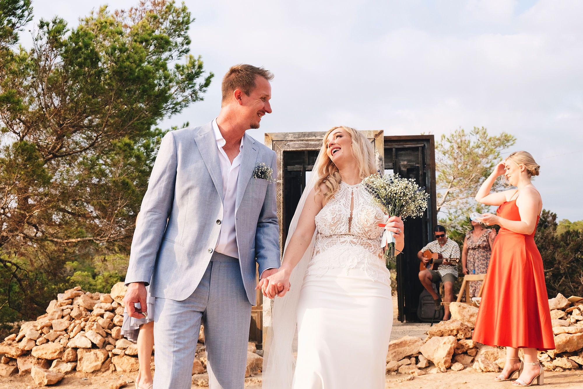 Bride and groom holding hands, walking, and laughing after the ceremony of their elopement in Spain at Cala Llentia, Ibiza