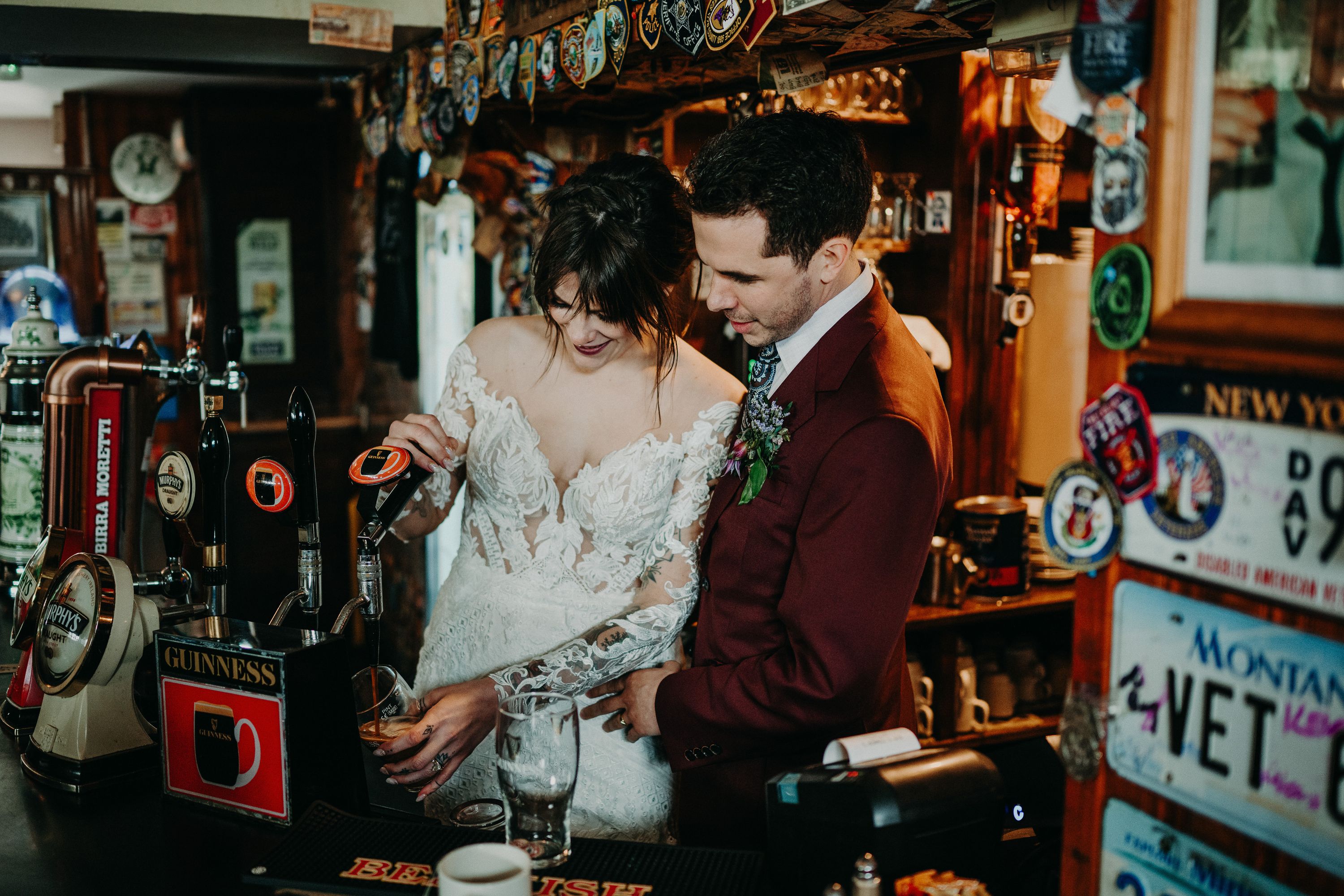A bride and groom pouring a drink onto a glass while they're inside a pub in Ireland