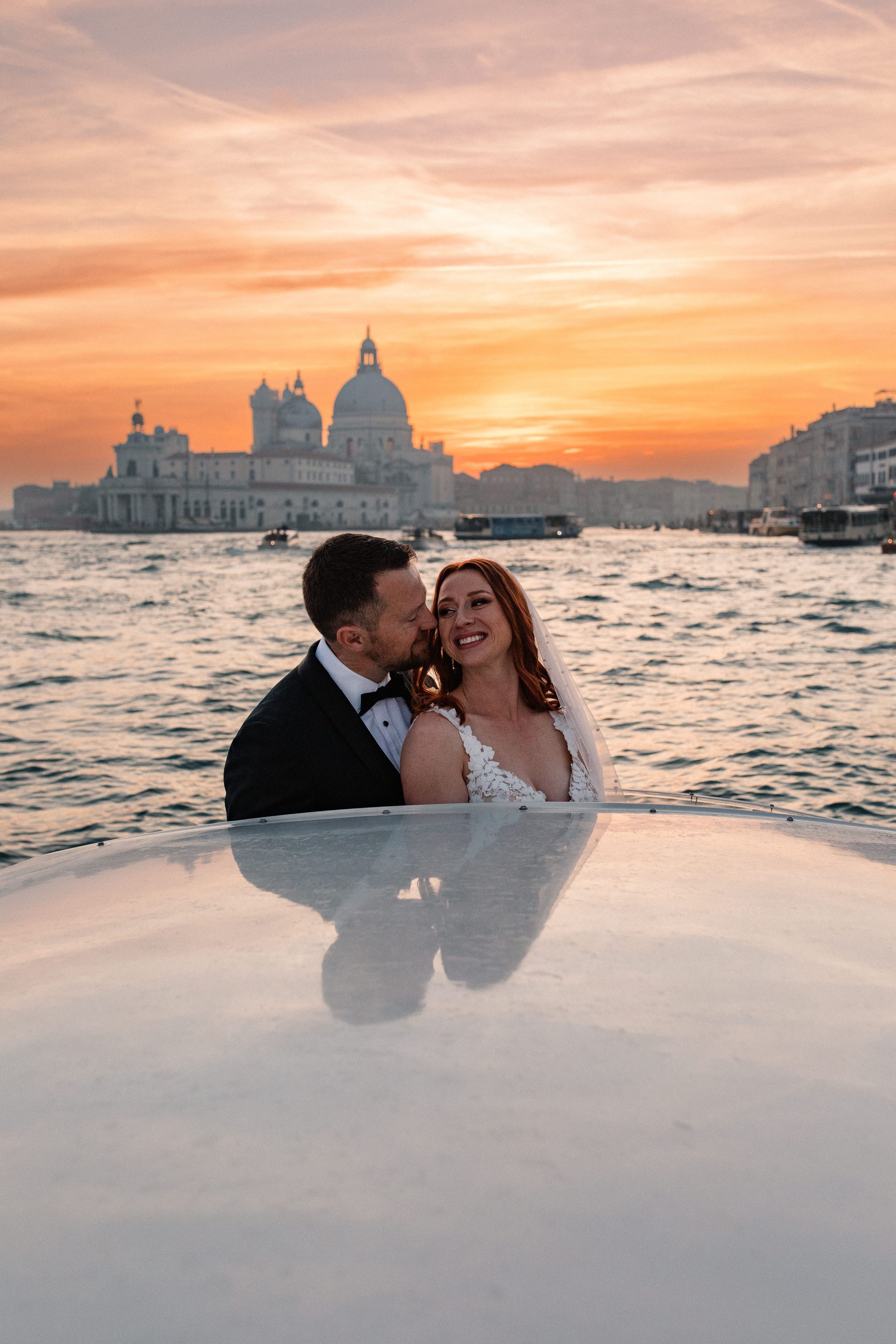 Groom kisses his bride on the cheek as they sail atop the Grand Canal for their elopement in Italy