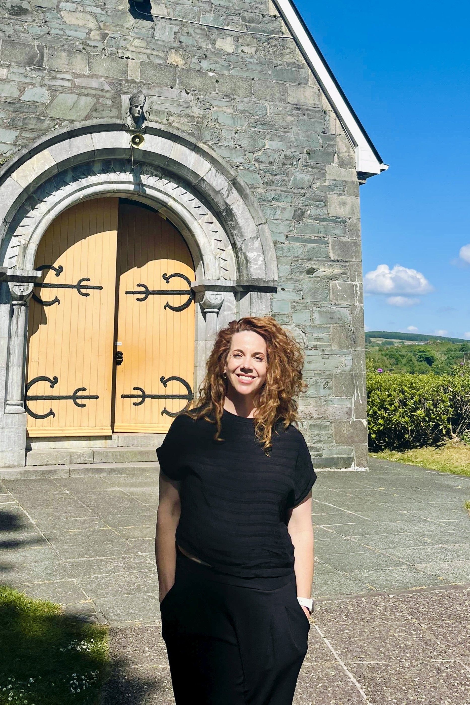 Our wedding planner in Ireland posing in front of a lakeside chapel in Gougane Barra