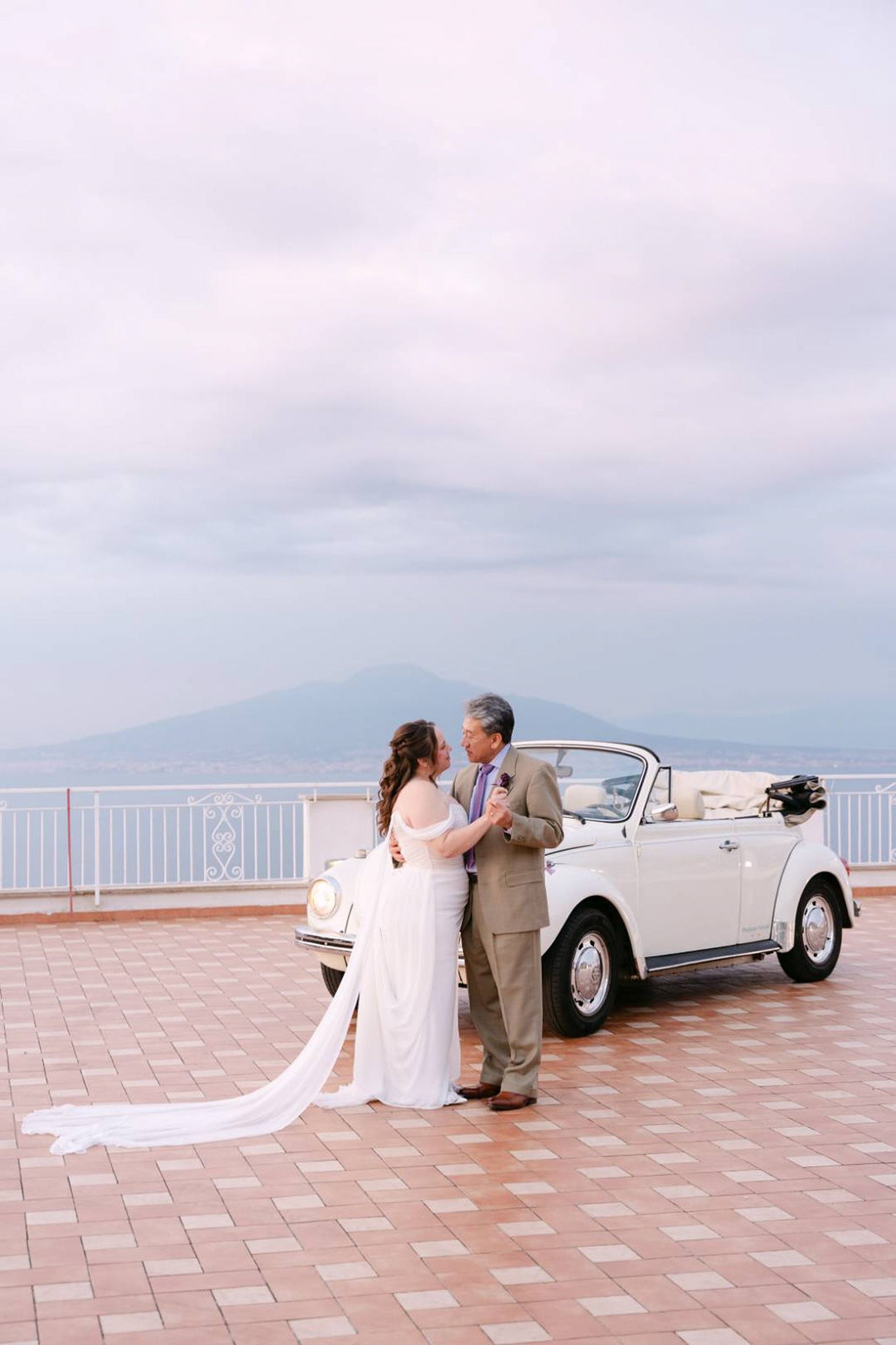 Couple share a dance beside a vintage car overlooking the sea at an intimate wedding in Italy