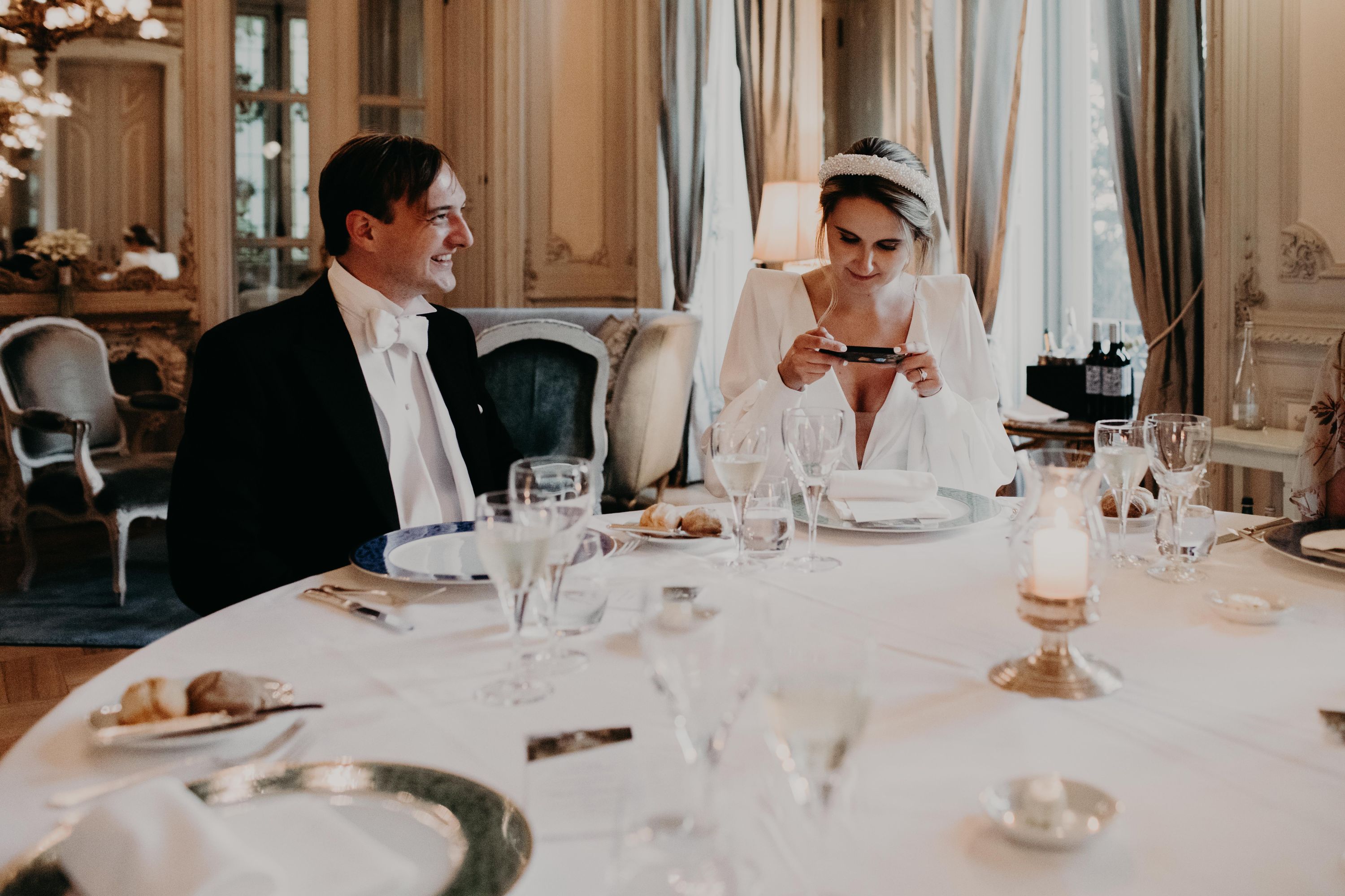 Bride takes photo of the food while seated on a round dining table with her groom
