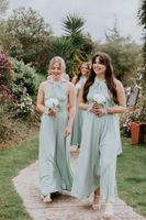 Bridesmaids wearing mint green dresses, holding white mini bouquets walk on a pathway to the ceremony area