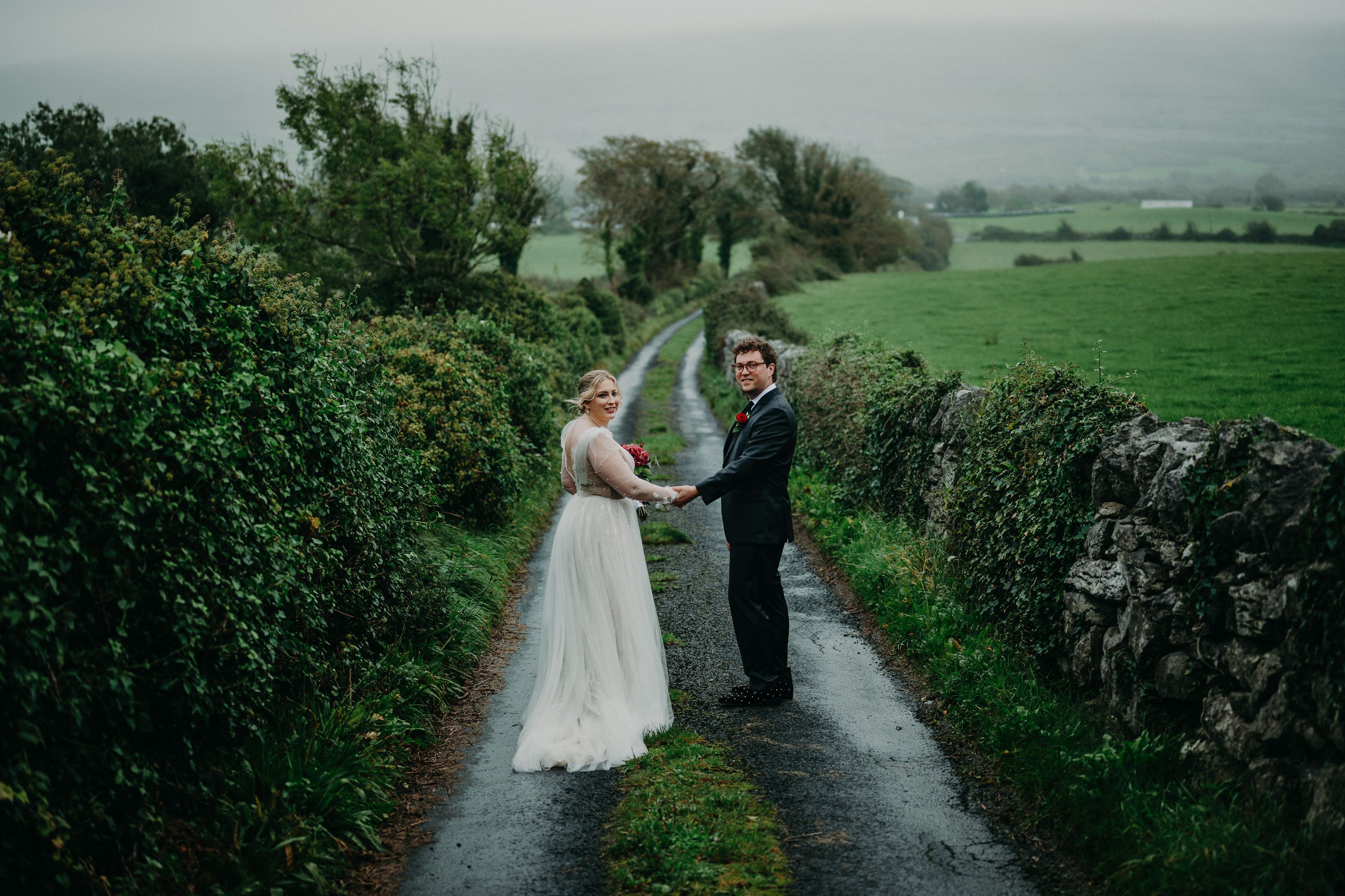 Newlyweds holding hands on a scenic rural road during an intimate wedding in Ireland portrait session