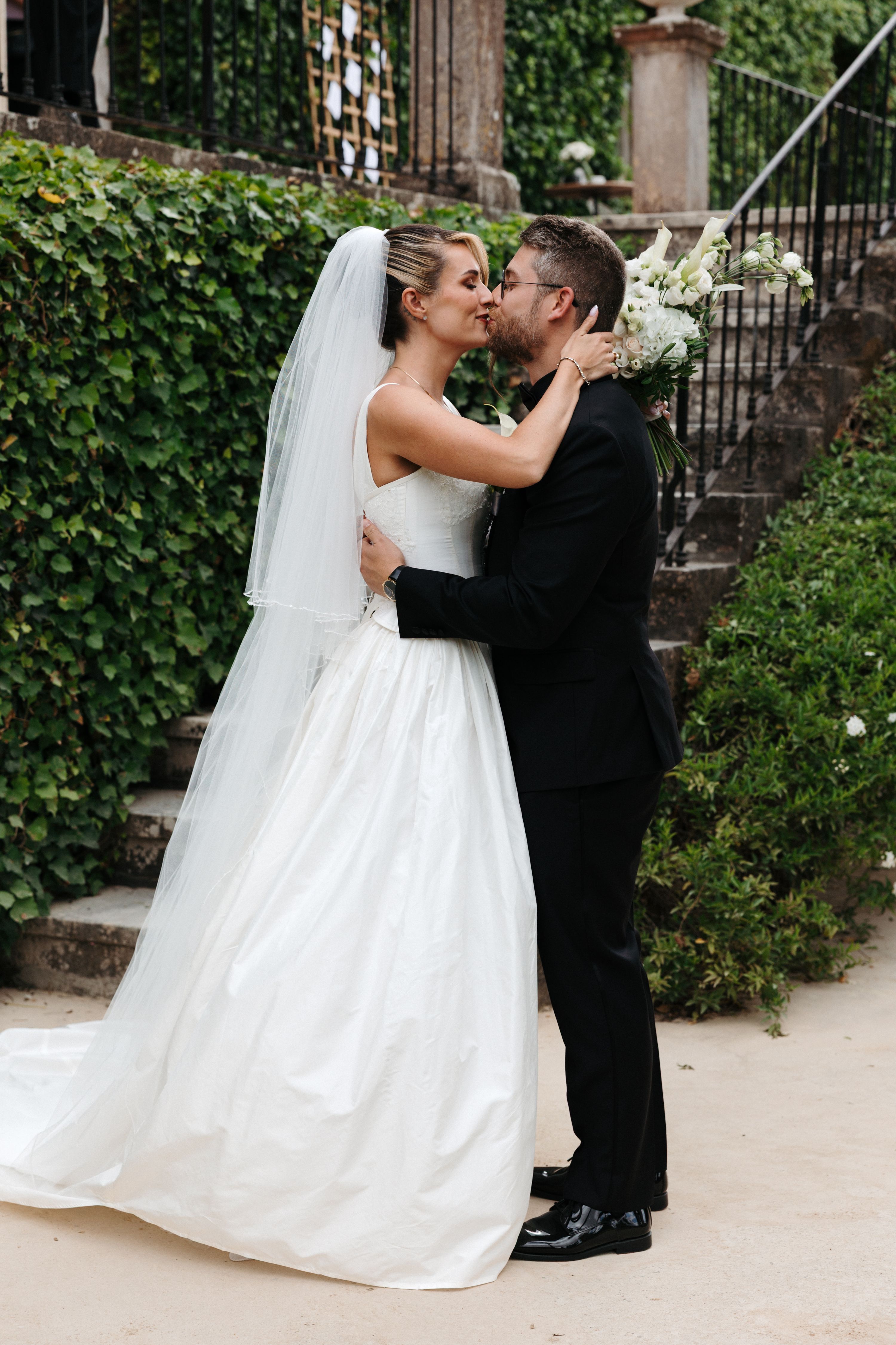 Groom and bride kissing in front of an ive-covered staircase