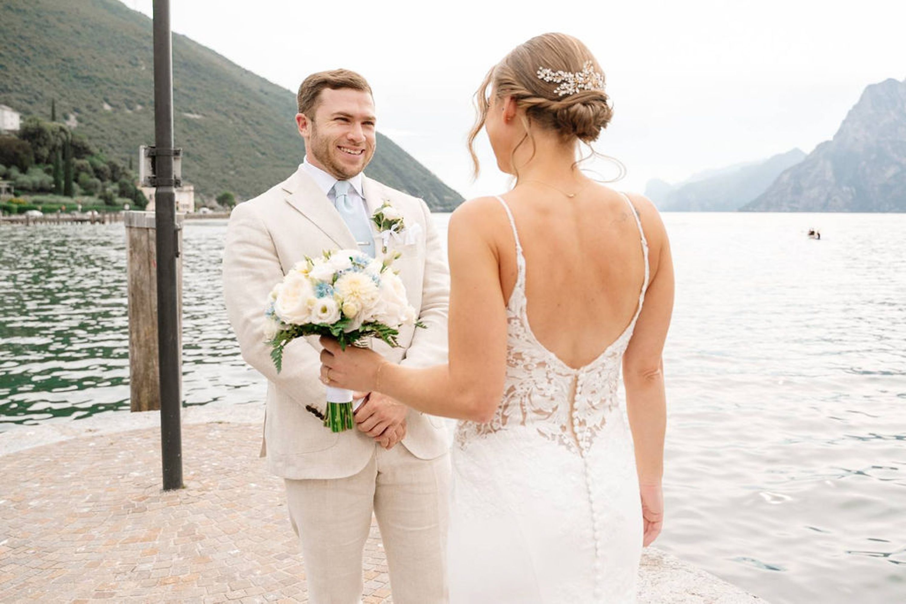 Groom presenting a bouquet to the bride beside a scenic lakeside during an intimate wedding in Europe