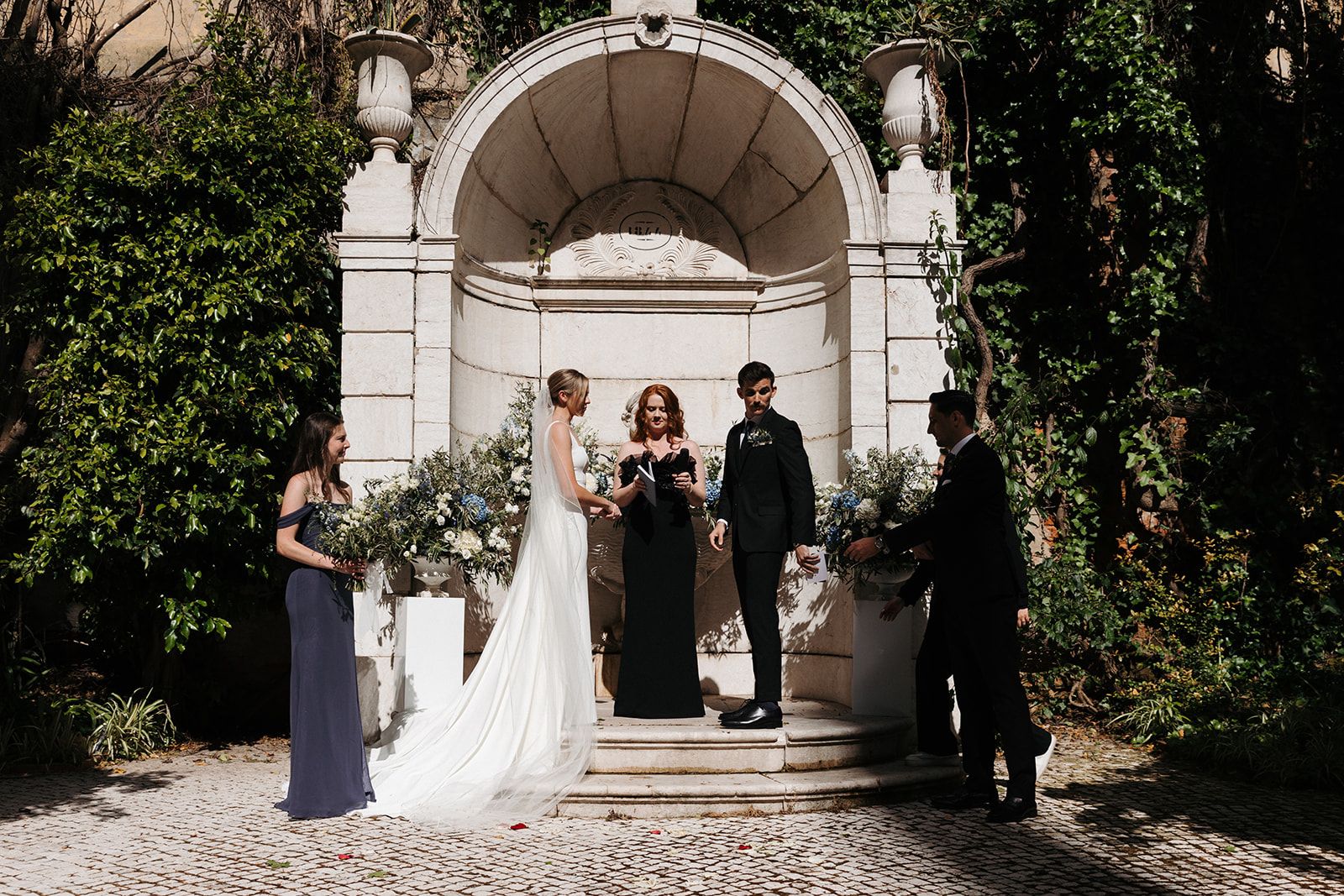 Couple having a wedding ceremony in a garden right inside a white gazebo during their destination wedding in Portugal