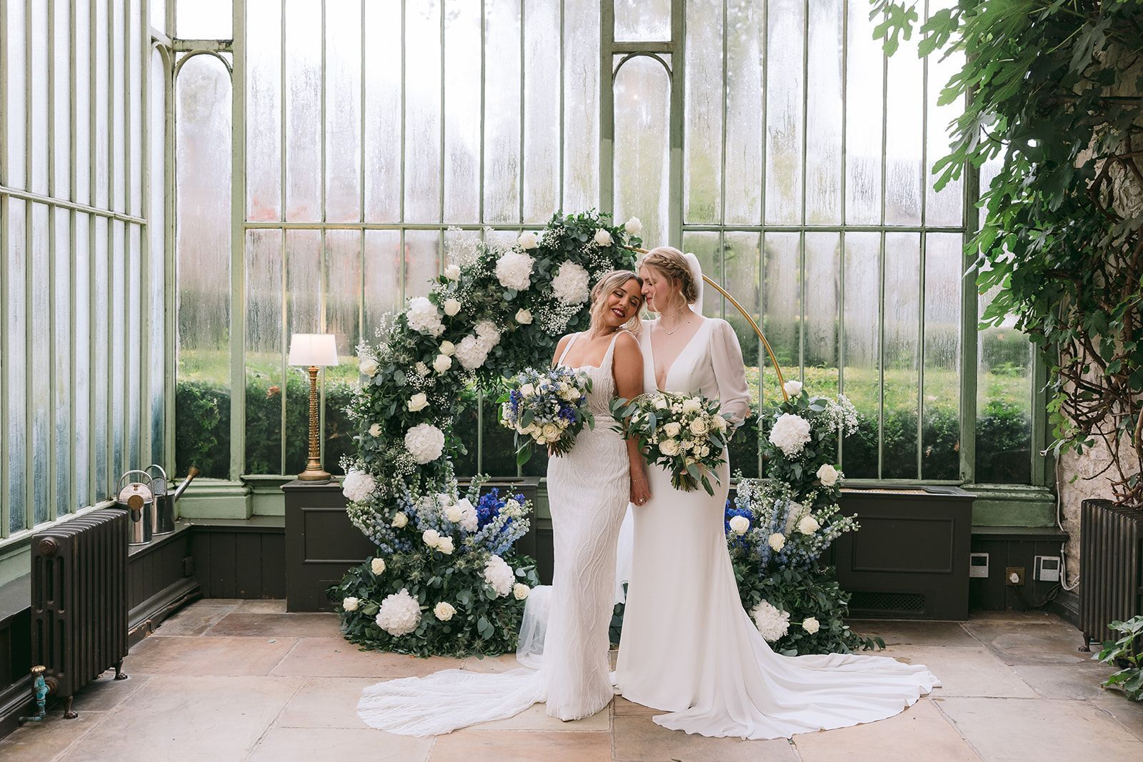 Two brides with a floral arch in the background inside a beautiful space during their destination wedding in Ireland