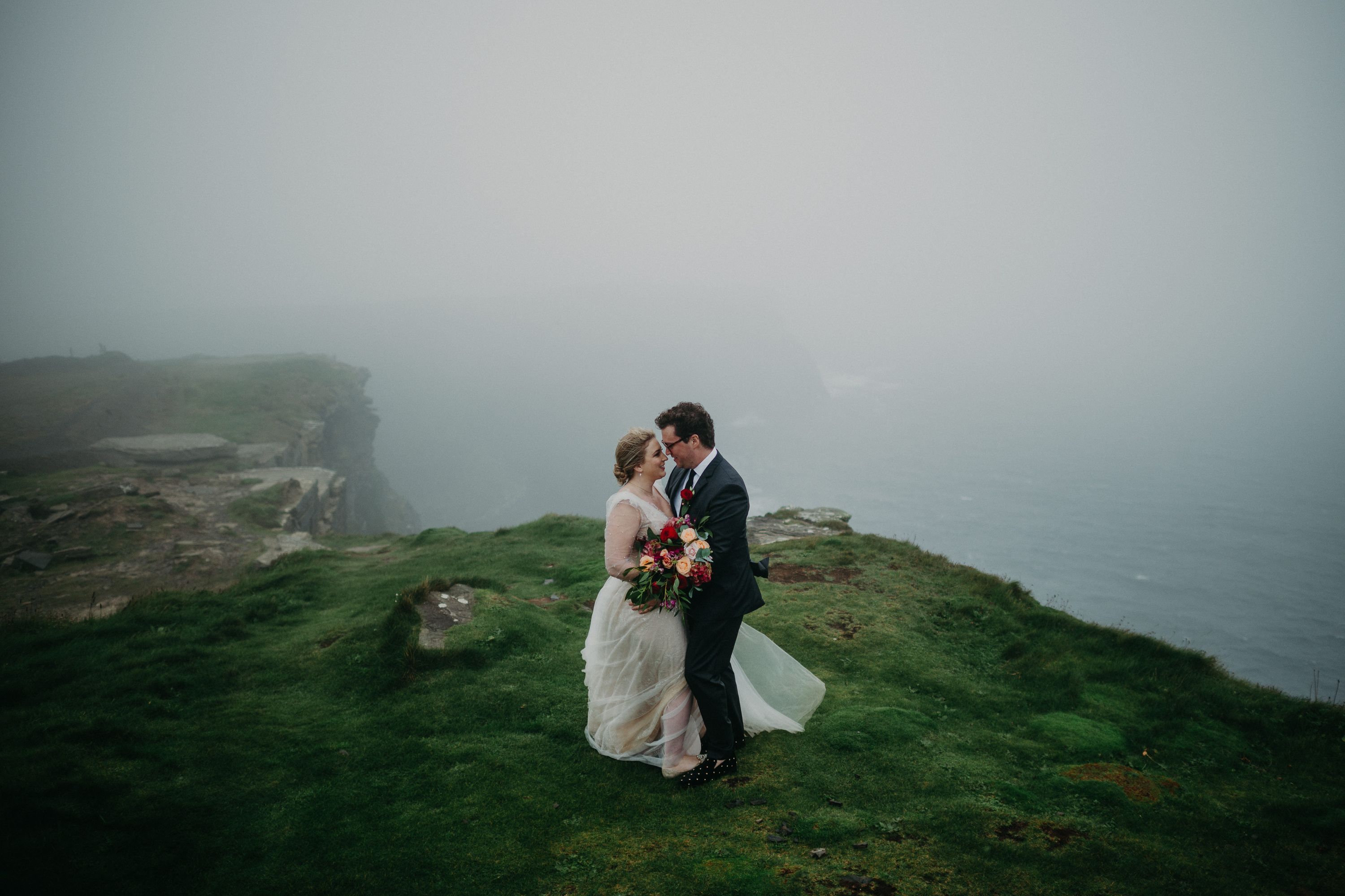 Bride and groom embracing on misty coastal cliffs during an intimate wedding in Ireland