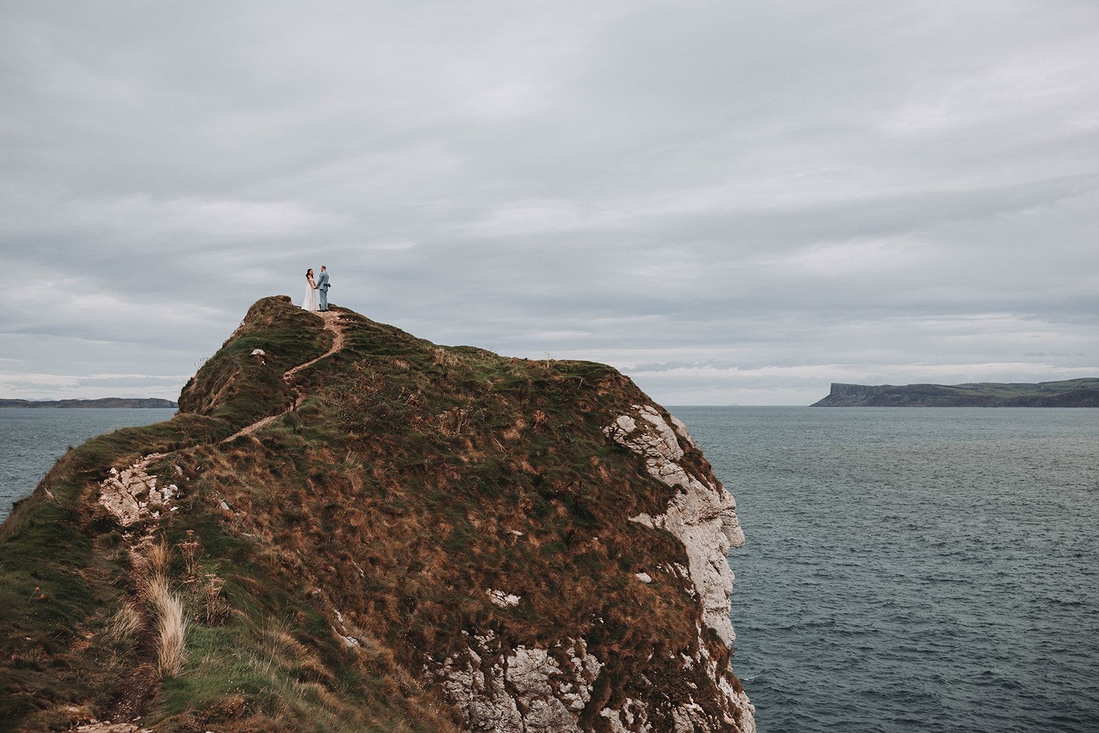 Newlyweds atop the cliffs having a photoshoot for their autumn Northern Ireland elopement with Atlantic Ocean as the backdrop