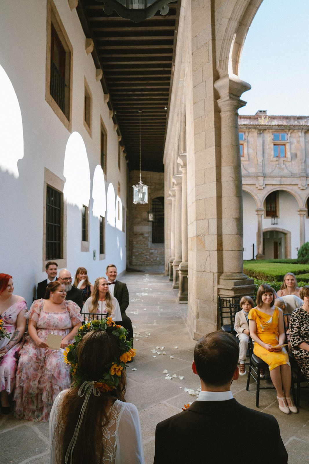 Bride in a sunflower crown and groom seen from behind during their small wedding ceremony in a cloister gallery in Santiago de Compostela.