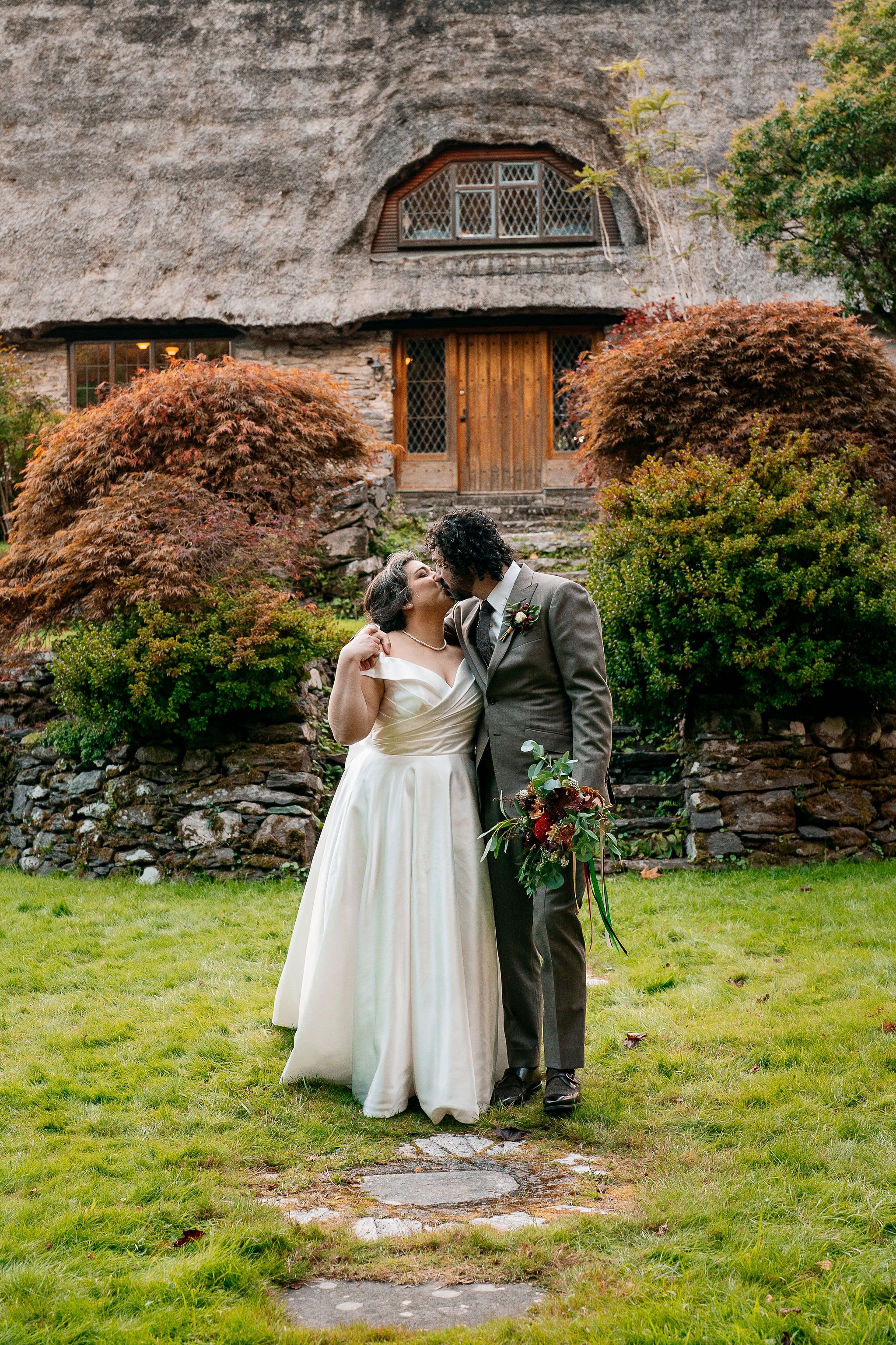 Bride and groom kissing with a thatched-roof cottage behind them during their elopement in Ireland