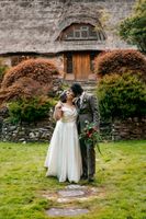Bride and groom kissing with a thatched-roof cottage behind them during their elopement in Ireland