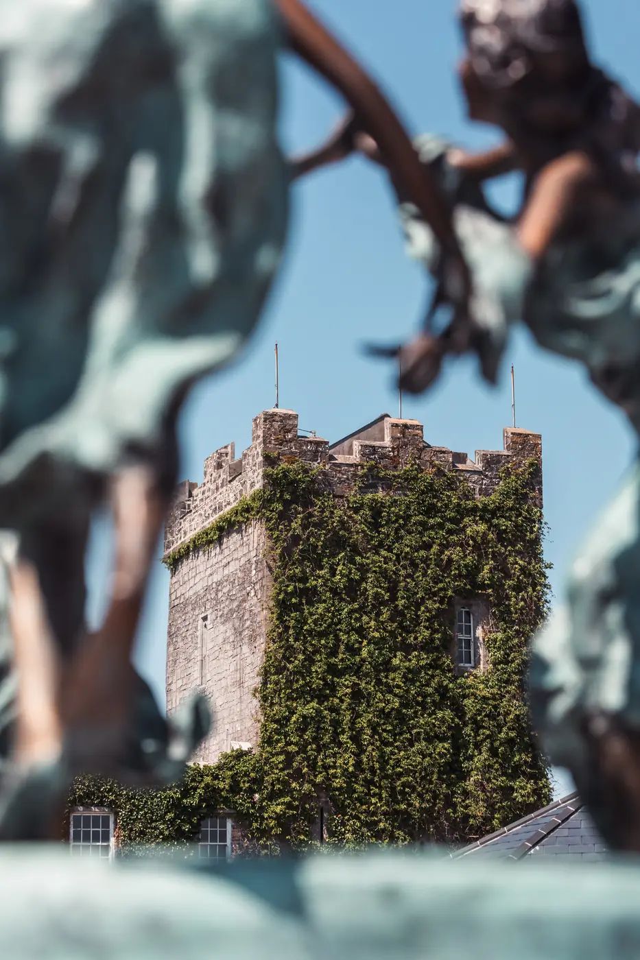 The battlemented tower of Cloonacauneen Castle framed between verdigris bronze statues on the forecourt.