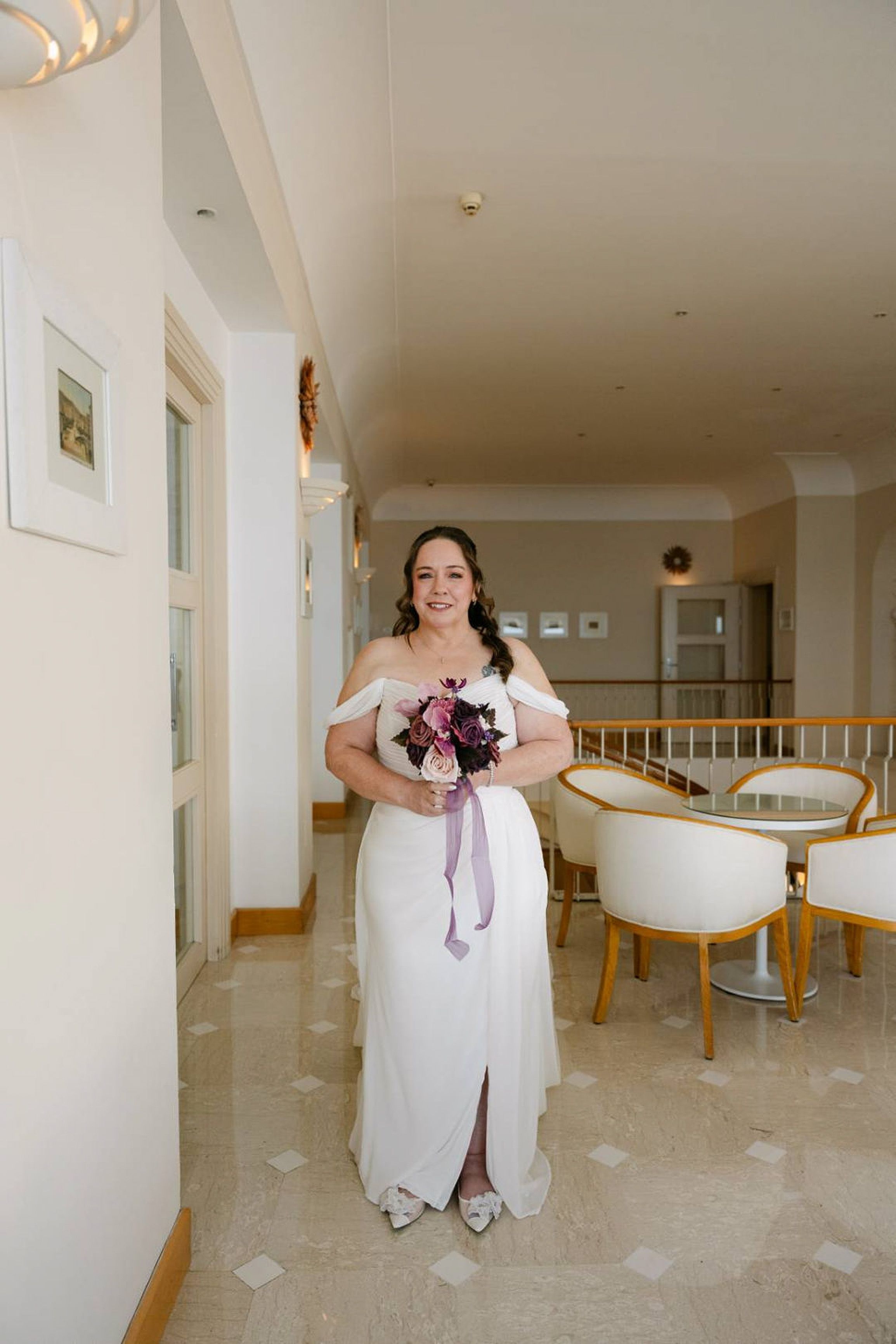 Bride standing in a bright hotel corridor holding a bouquet for a small wedding in Italy
