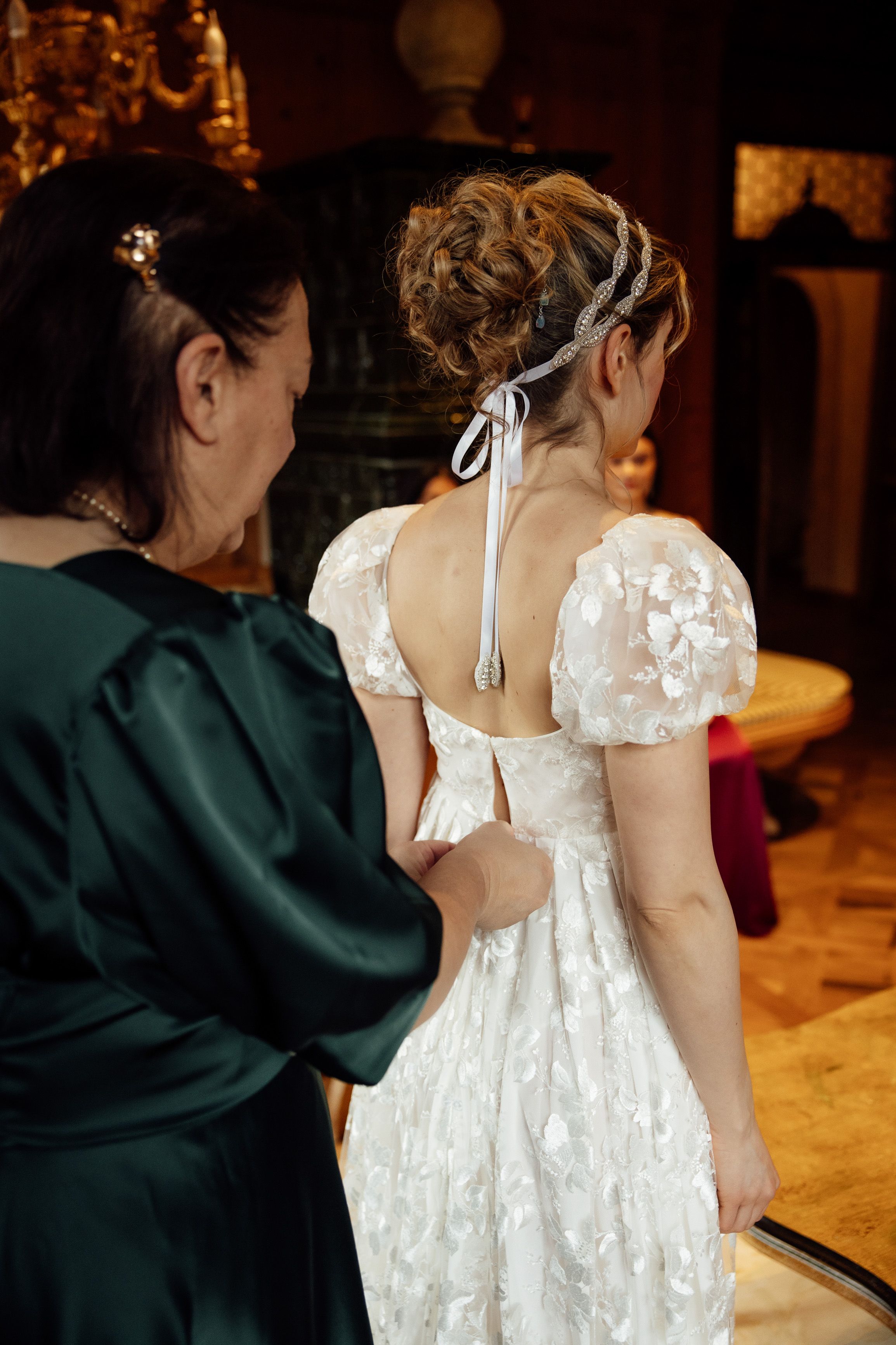 Bride's mother helps button her lace gown before an intimate wedding in Austria