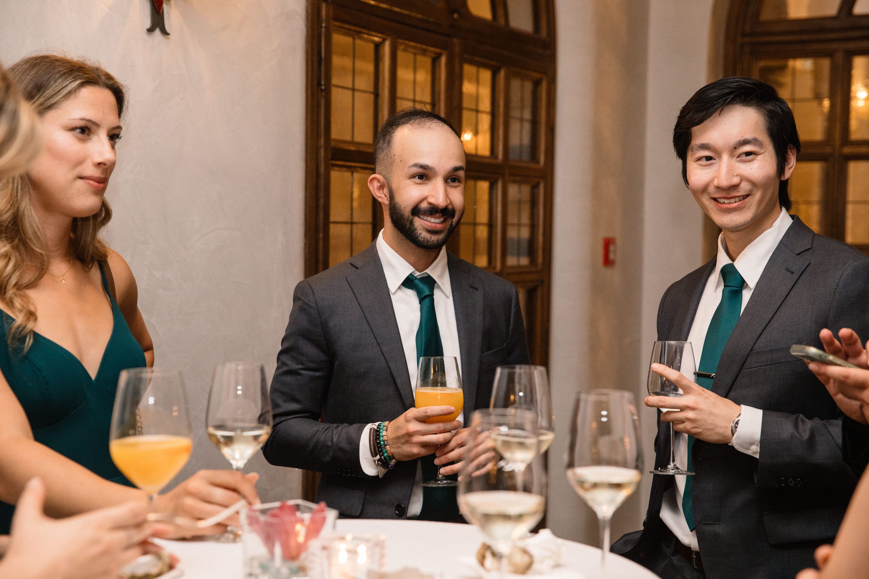 Two male and one female wedding guests holding champagne glasses and smiling