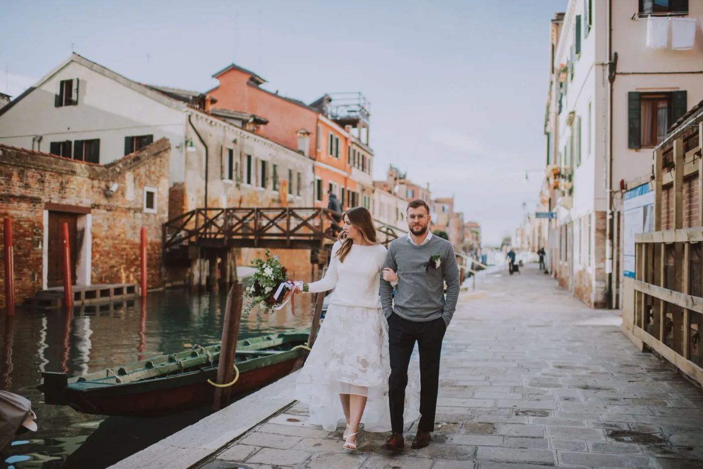 Couple wearing casual clothes walking along the banks of the Grand Canal after the ceremony of their elopement in Italy