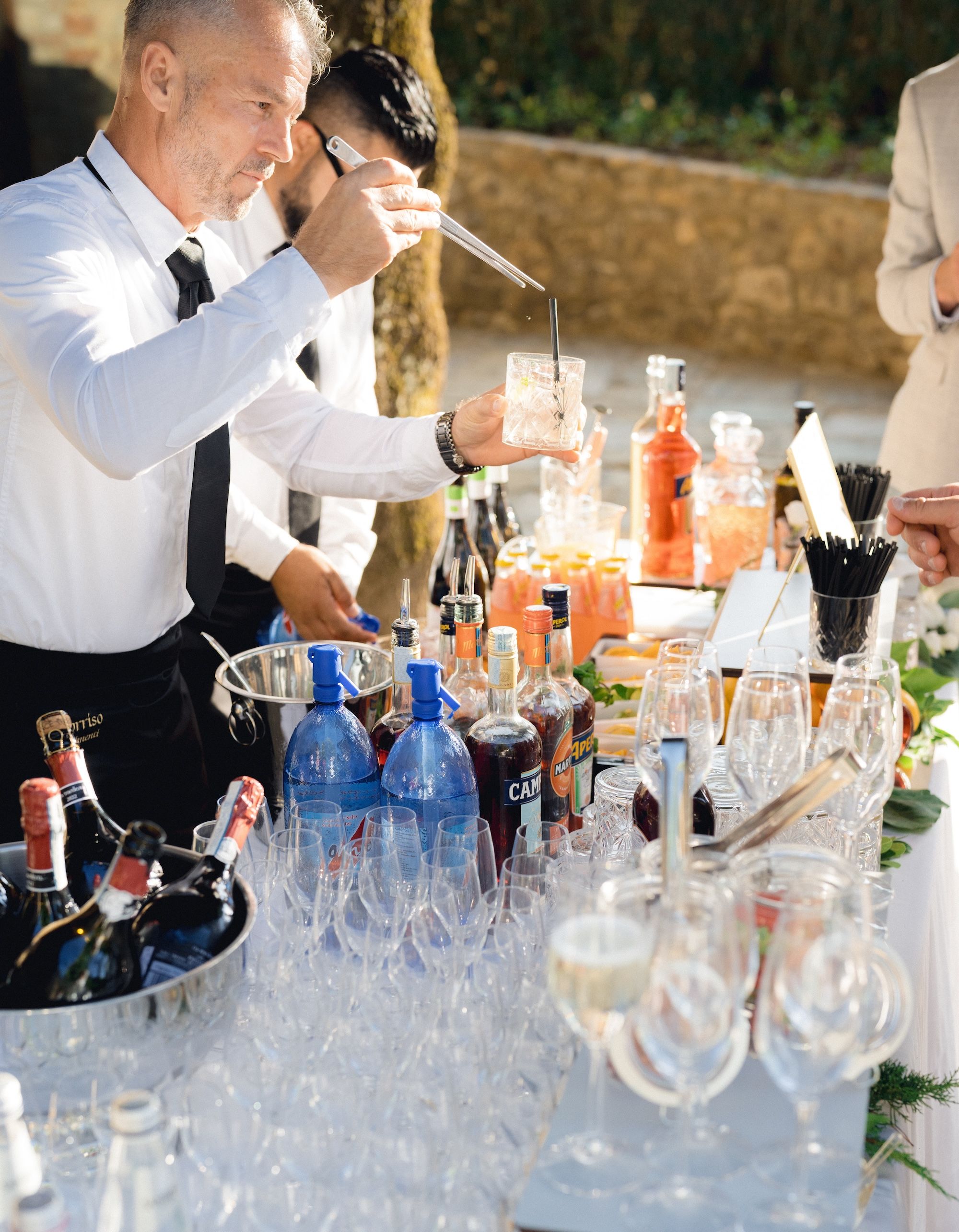 A bartender holds a glass as he creates drinks with many liquor bottles in front of him during a drinks reception