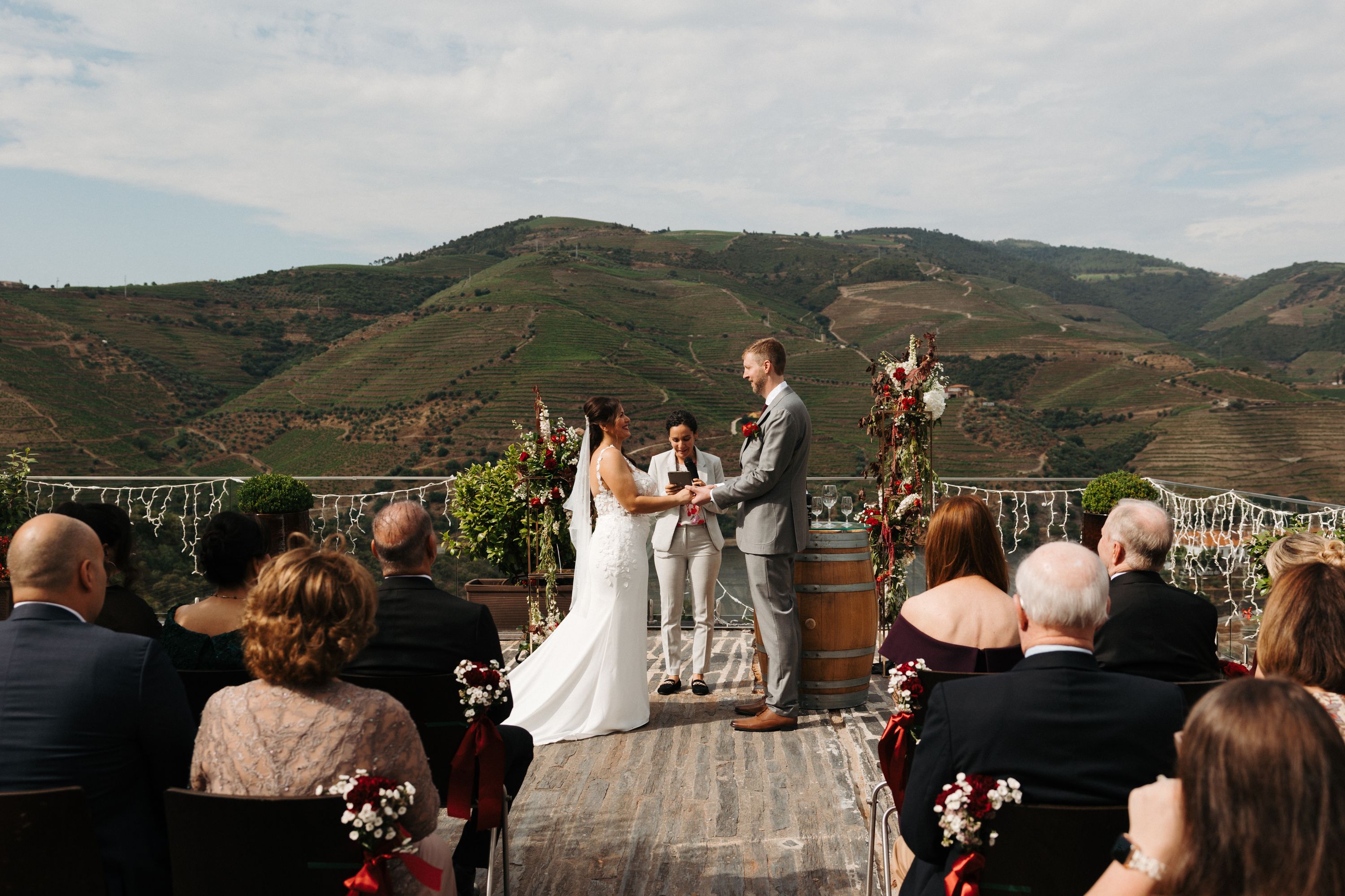 Bride and groom hold hands in a ceremony atop a terrace with a mountain backdrop during their destination wedding in Portugal