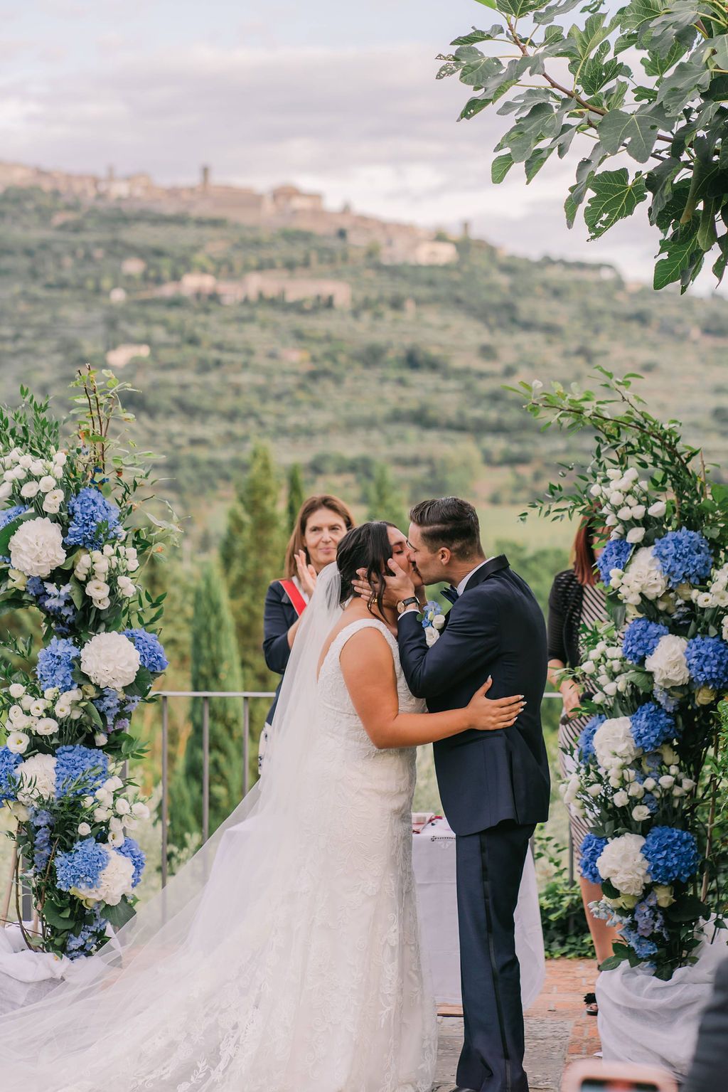 Bride and groom kiss in front of their celebrant with the rolling hills in the background during their small wedding in Tuscany