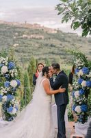 Bride and groom kiss in front of their celebrant with the rolling hills in the background during their small wedding in Tuscany