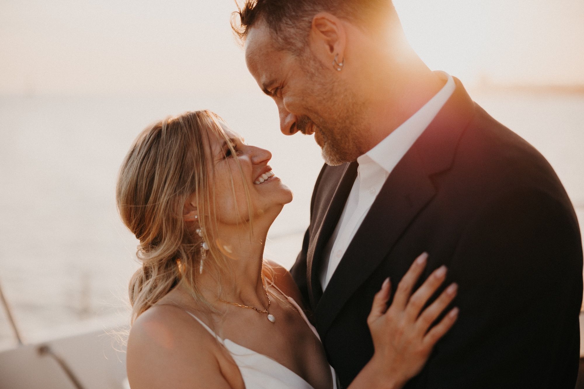 Bride and groom looking at each other and hugging with sunset behind them during their destination wedding in Portugal