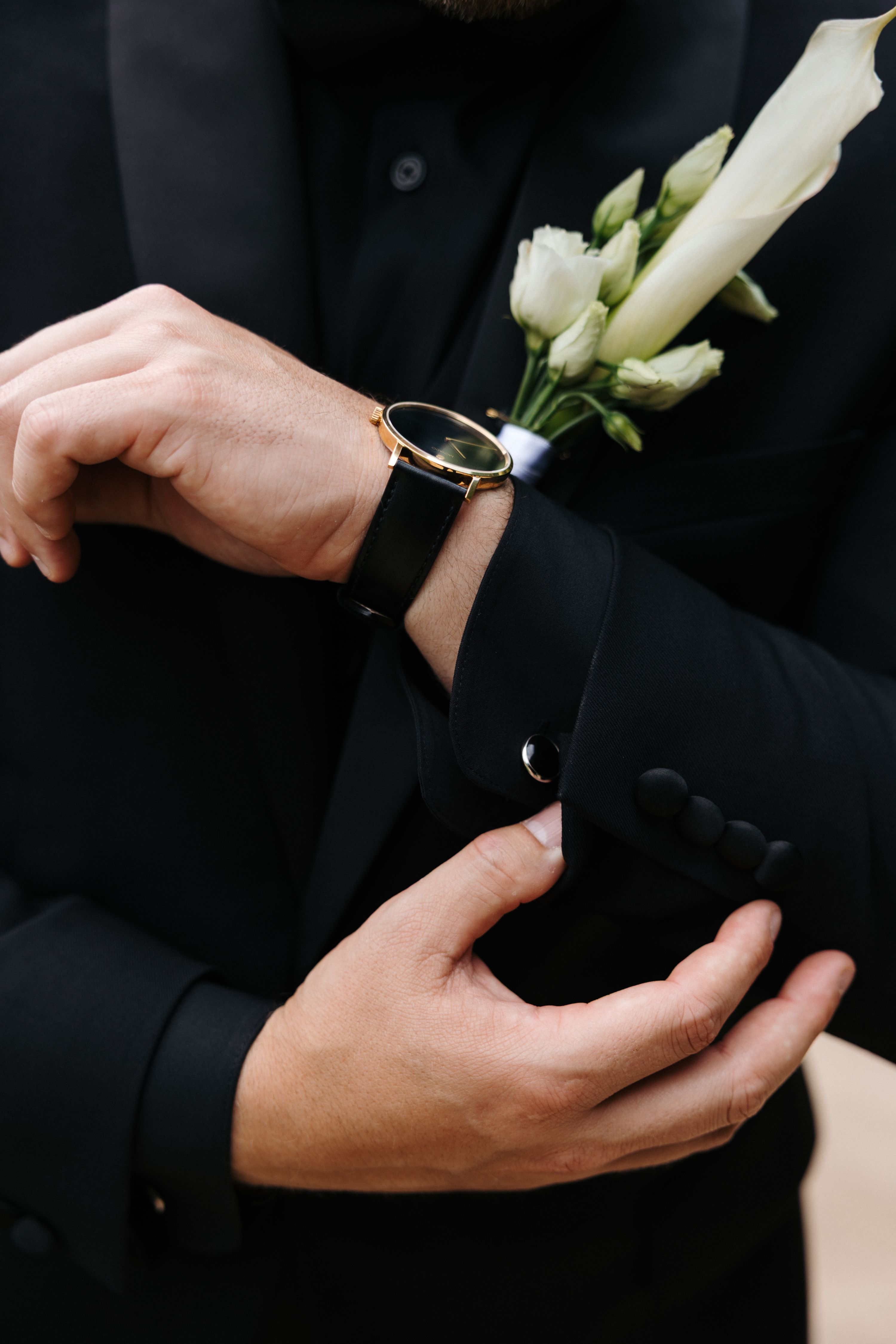 Closeup of an elegant black groom outfit with watch and boutonnière visible