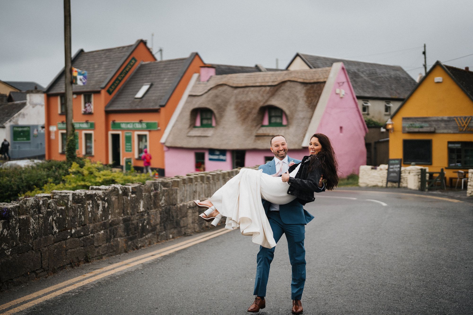 Groom carrying his bride in a colorful village after their wedding in Ireland