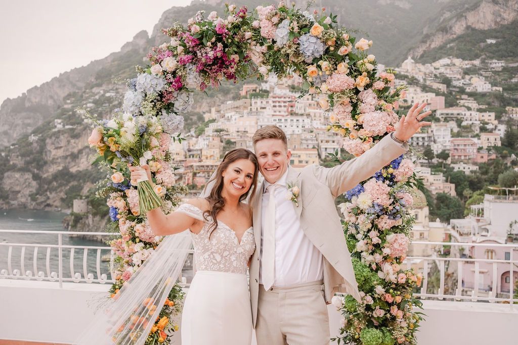 Bride and groom posing under a floral arch on a terrace in Amalfi Coast