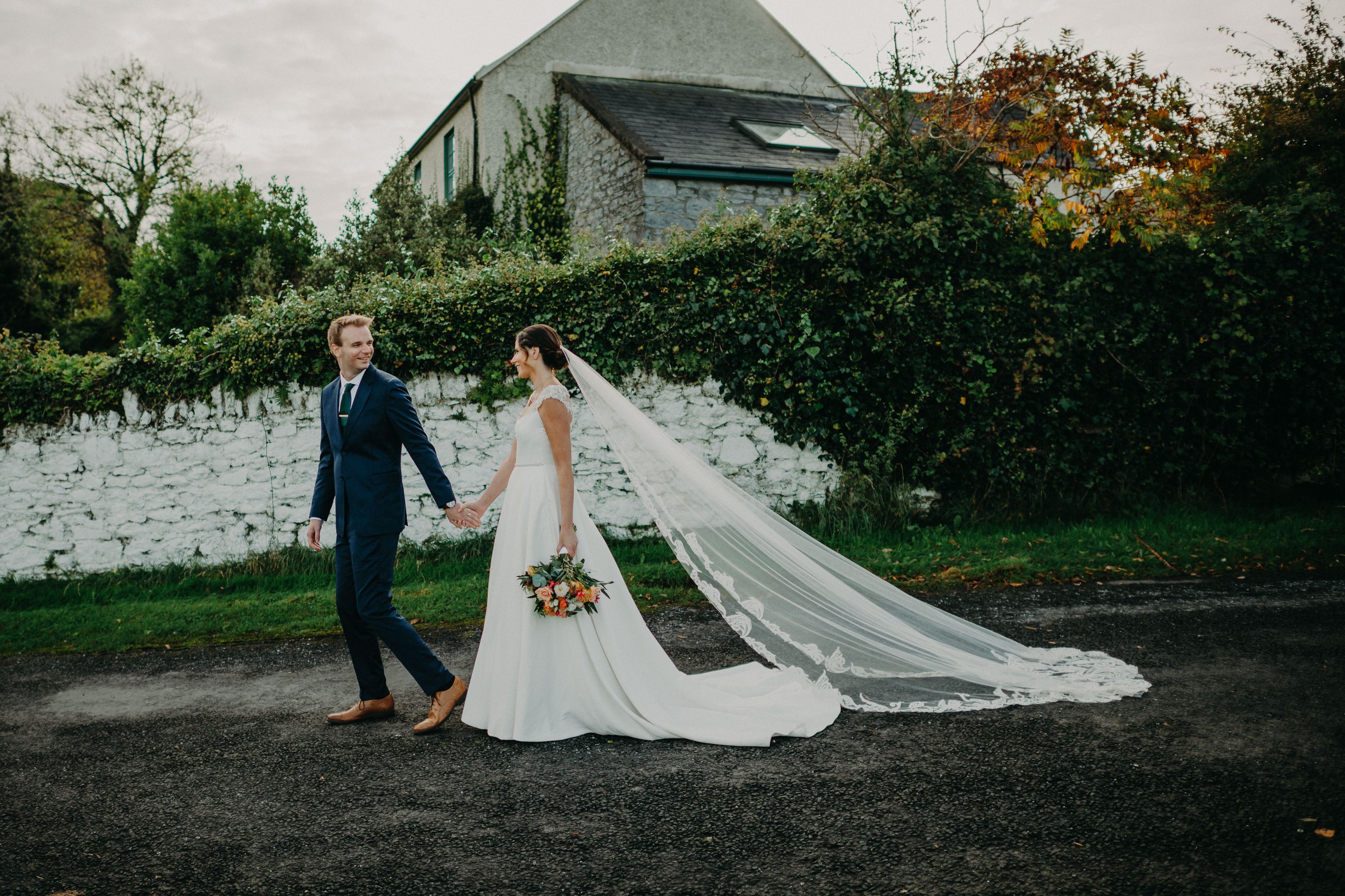 Newlyweds posing by a stone garden wall after an intimate wedding in Ireland at a countryside castle venue.