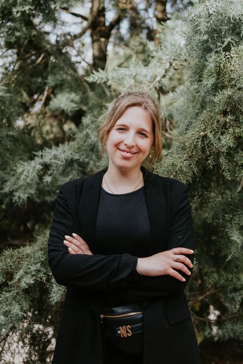 Our wedding planner in Portugal smiling, wearing a black shirt and blazer with greenery in the background