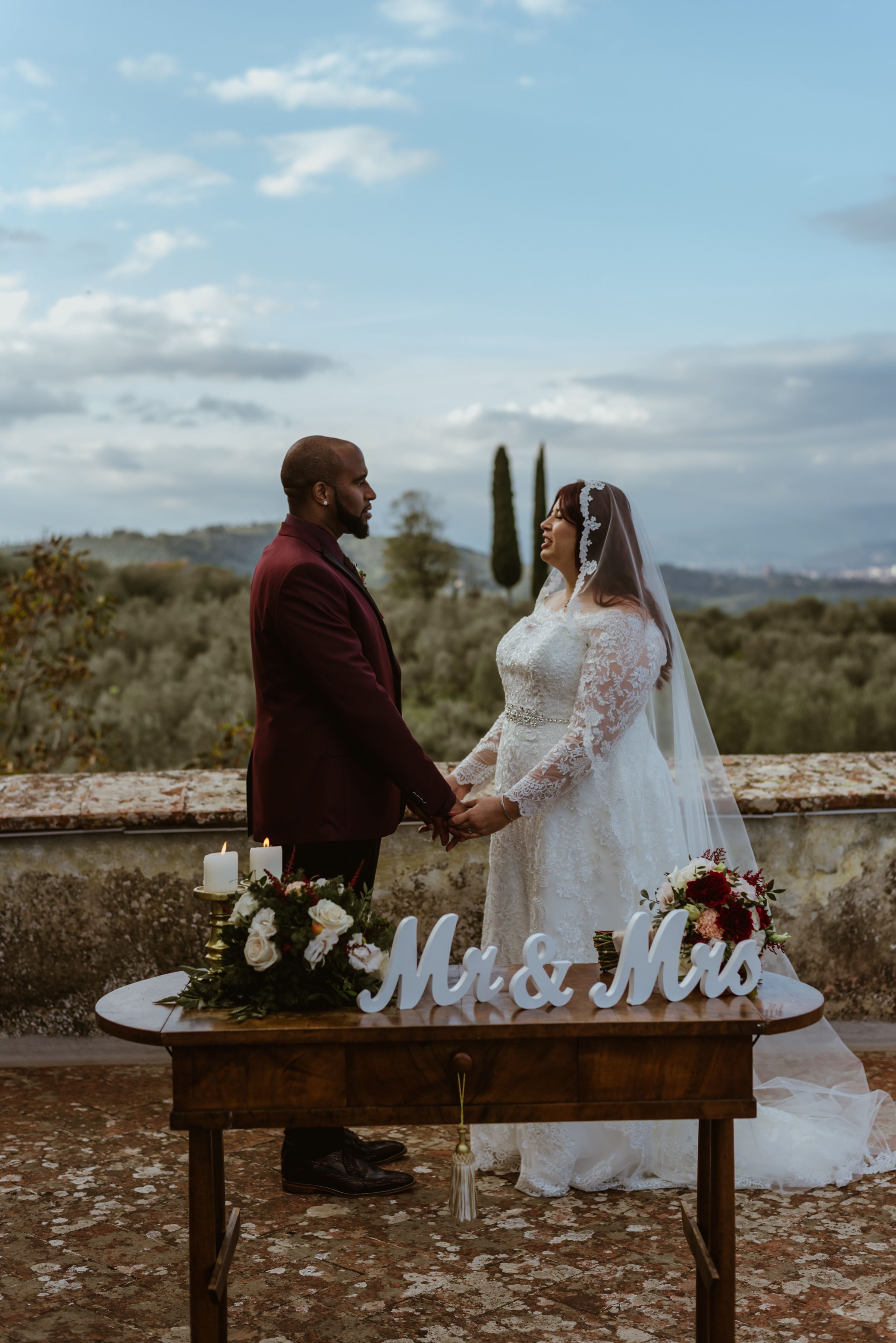 Bride and groom holding hands during their destination wedding ceremony in Italy with Tuscan views in the background