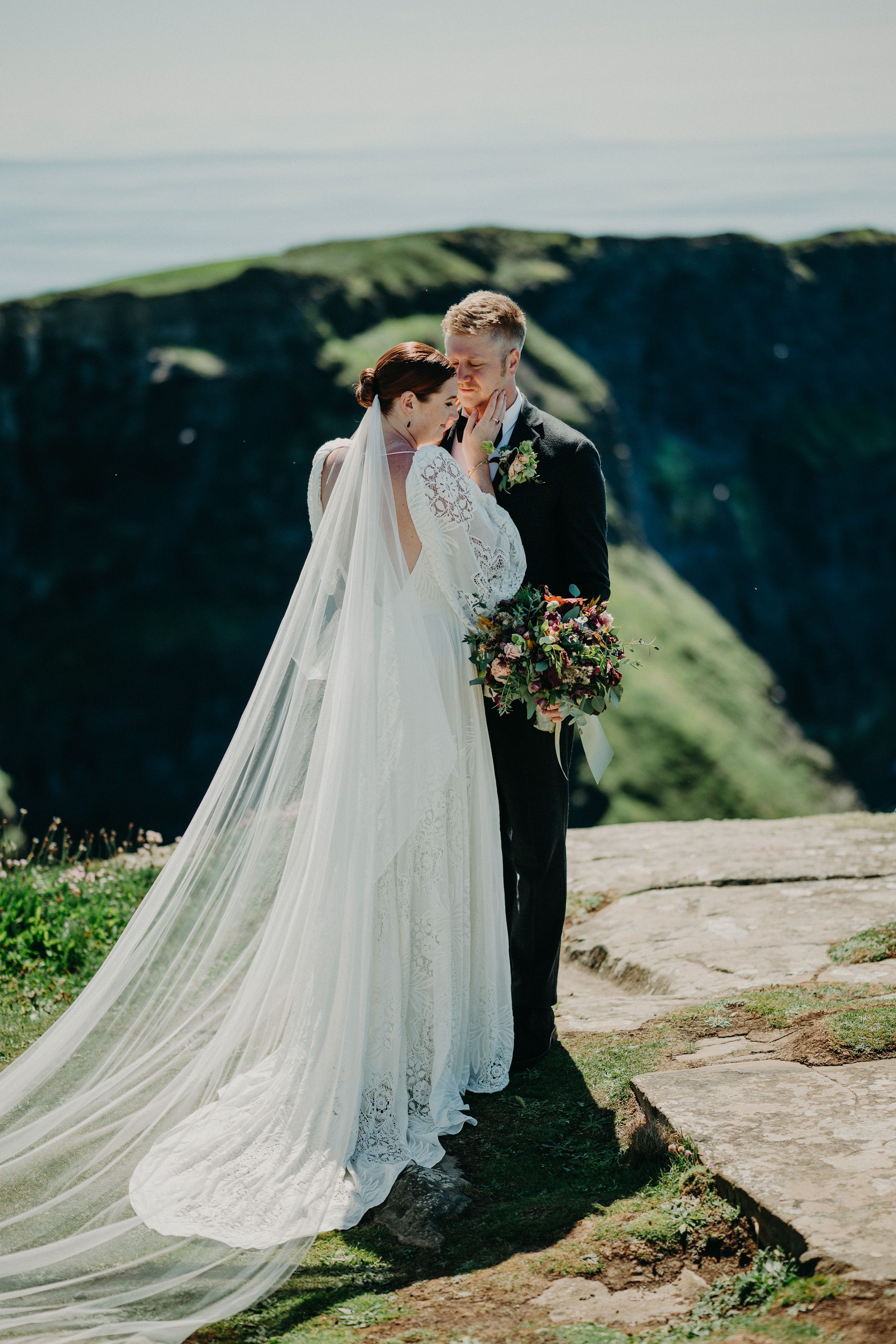 A bride and groom sharing a quiet moment on top of a stunning cliff with beautiful views of the sea after their small wedding in Ireland