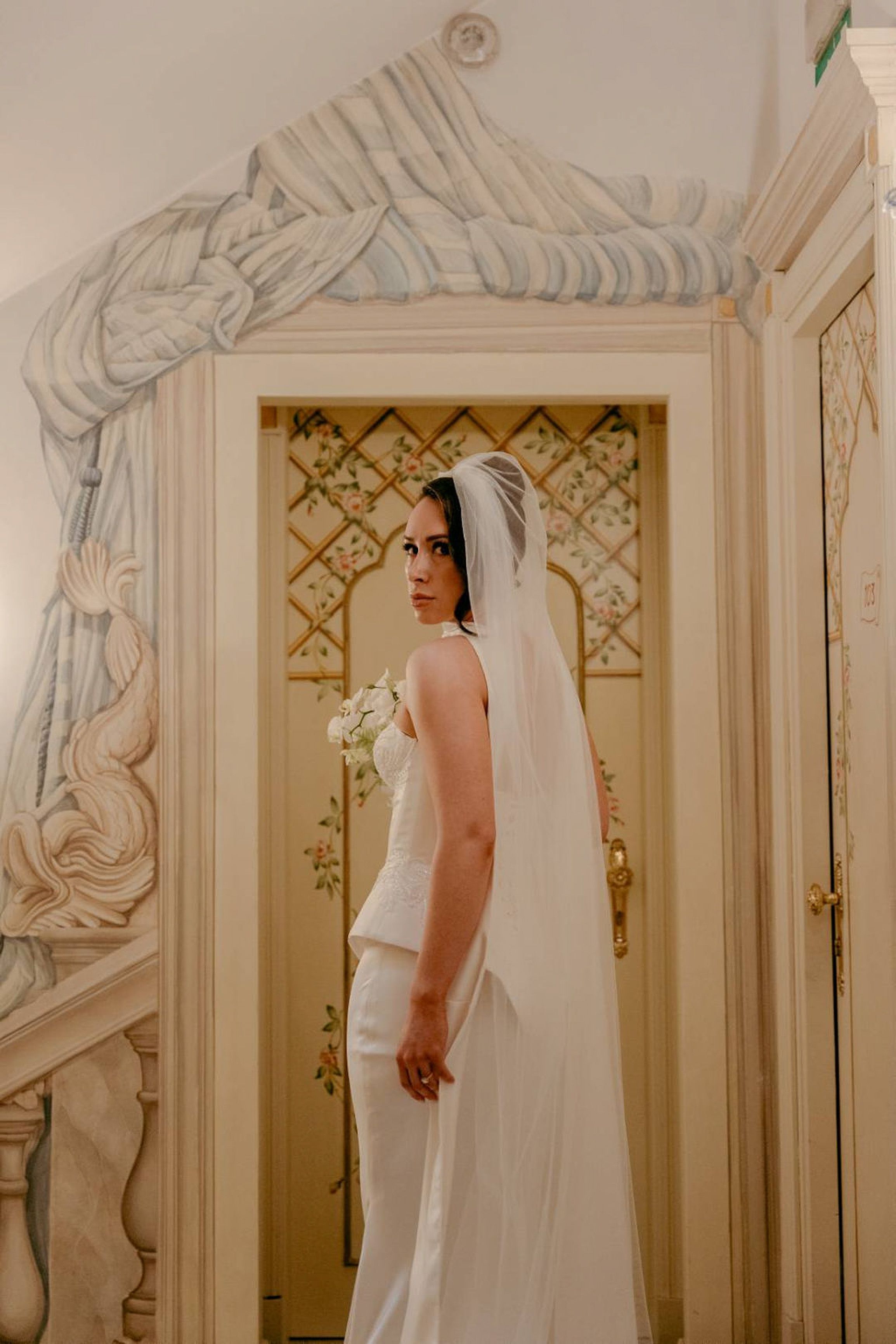 Bride standing in an ornate hallway with a flowing veil at a small wedding in Italy