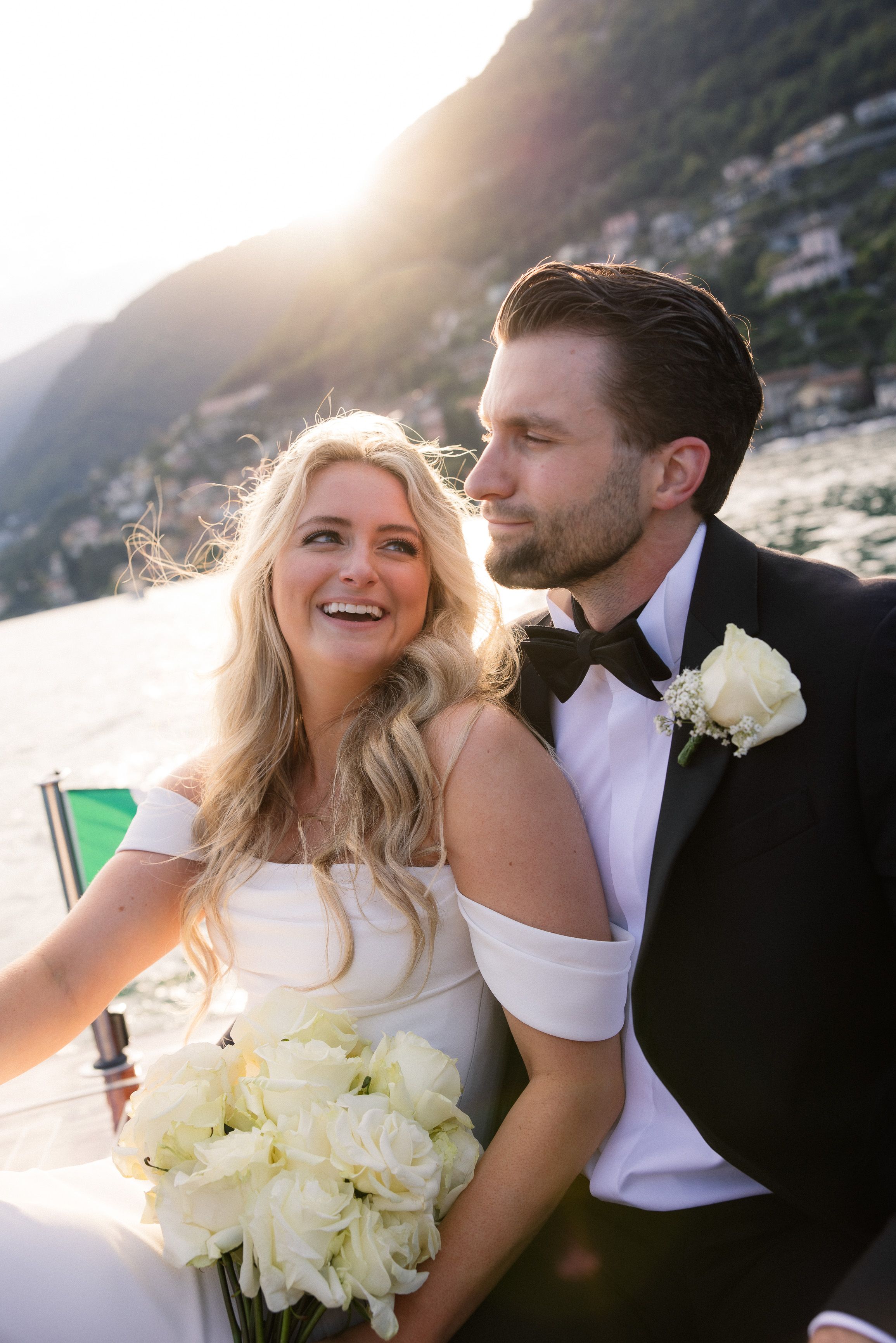 A bride gazing at her groom while they are traversing a beautiful lake with the mountain behind them for their small wedding in Italy