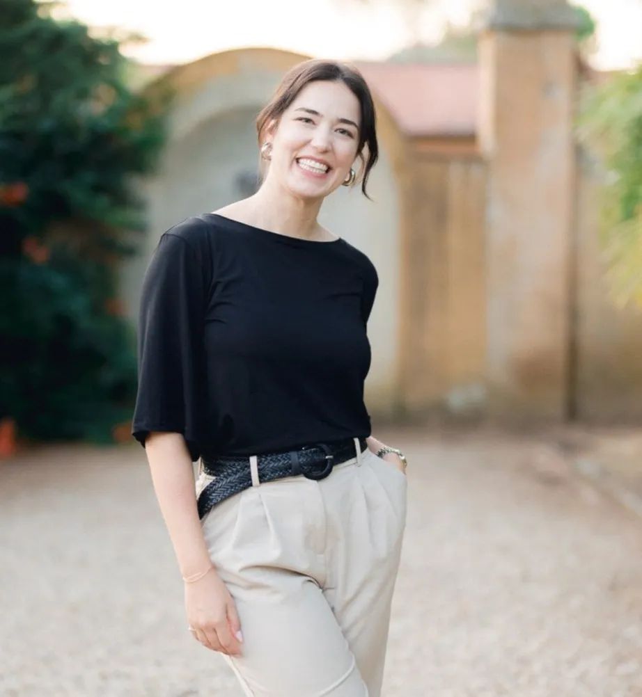 Wedding planner in Italy standing and smiling in front of the camera with a medieval stone wall in the background.