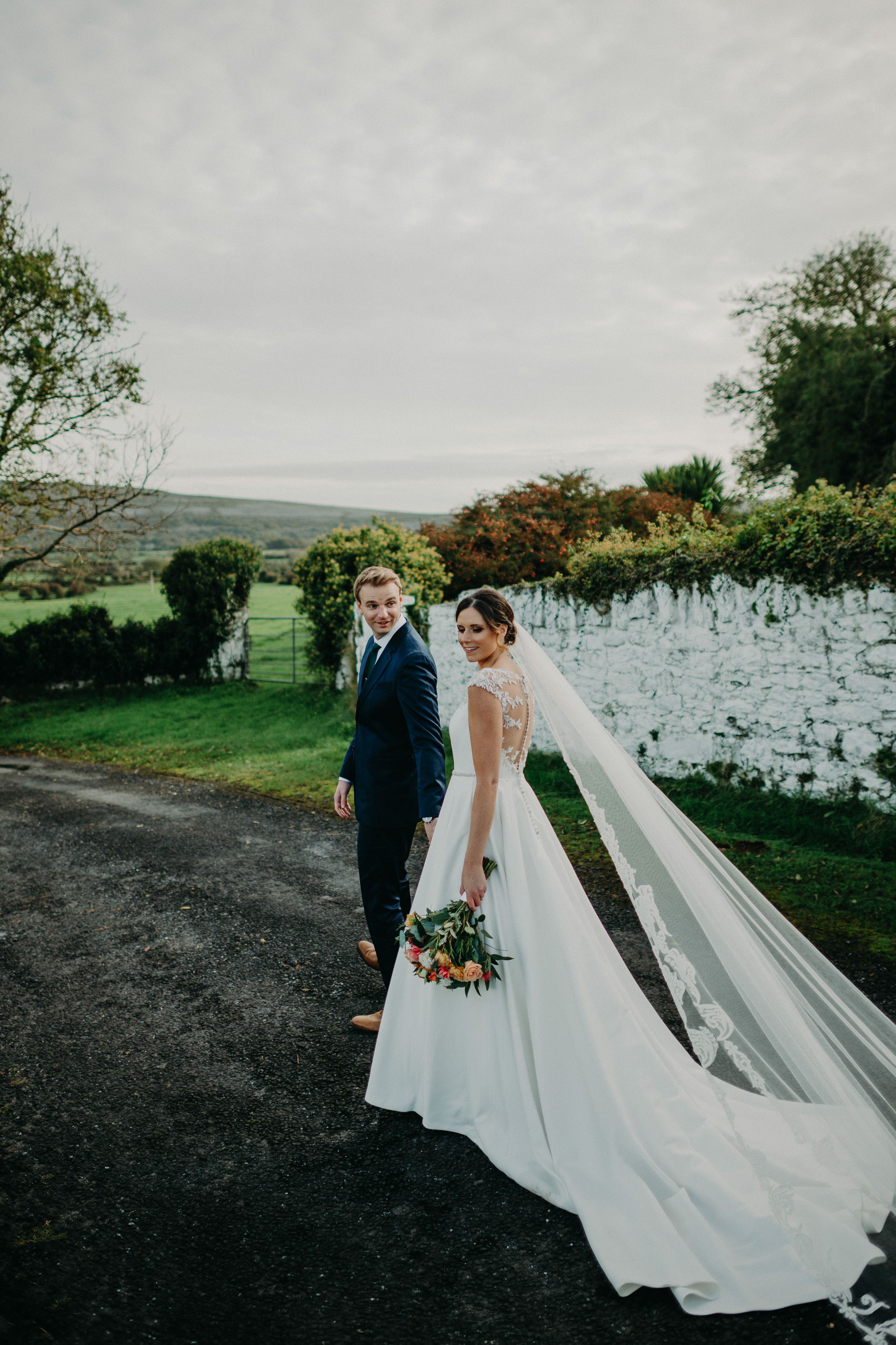 Small wedding in Ireland with bride and groom walking outdoors by a stone wall on a cloudy day