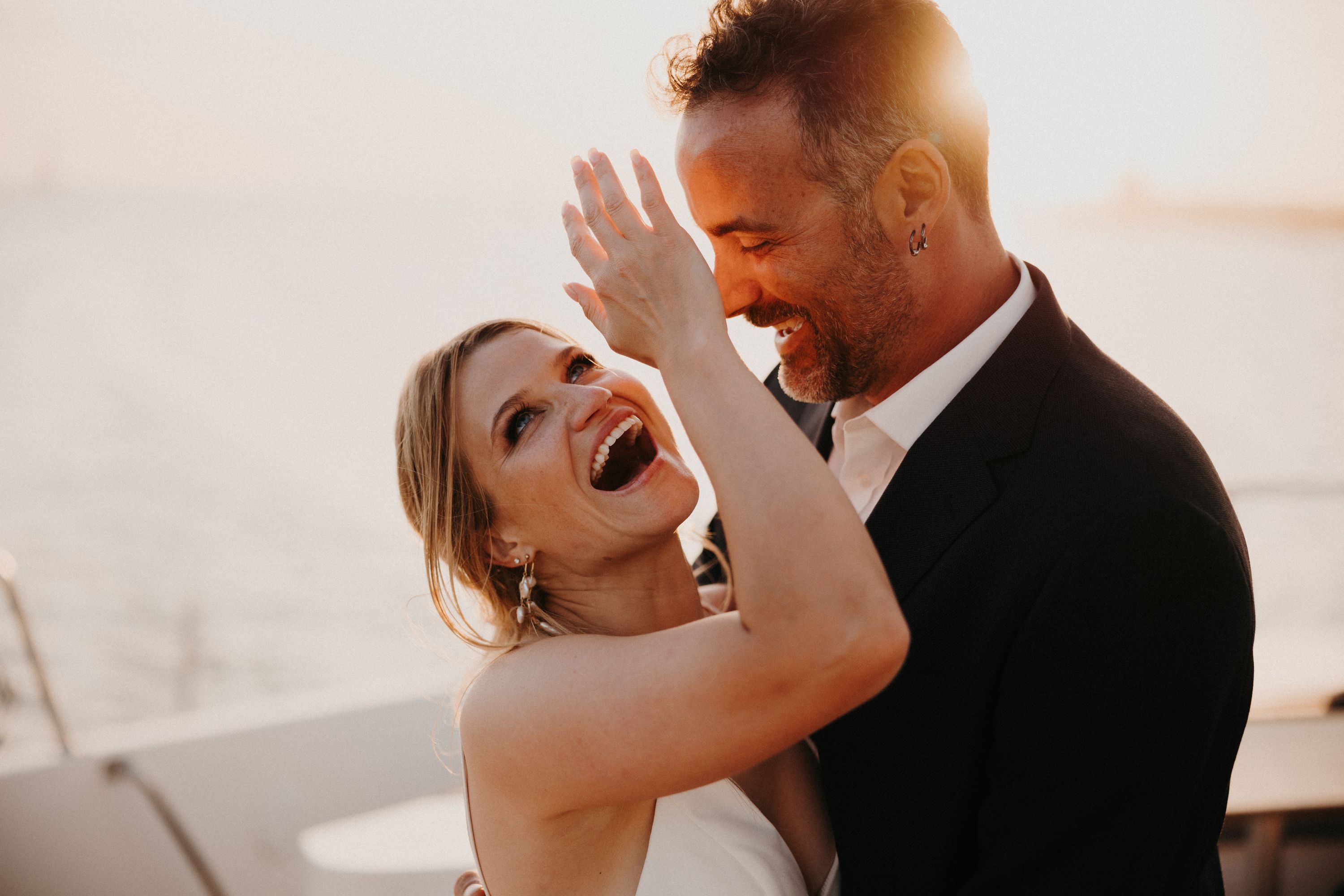Bride and groom laughing and hugging each other during their sunset destination wedding in Portugal, with sea as the backdrop