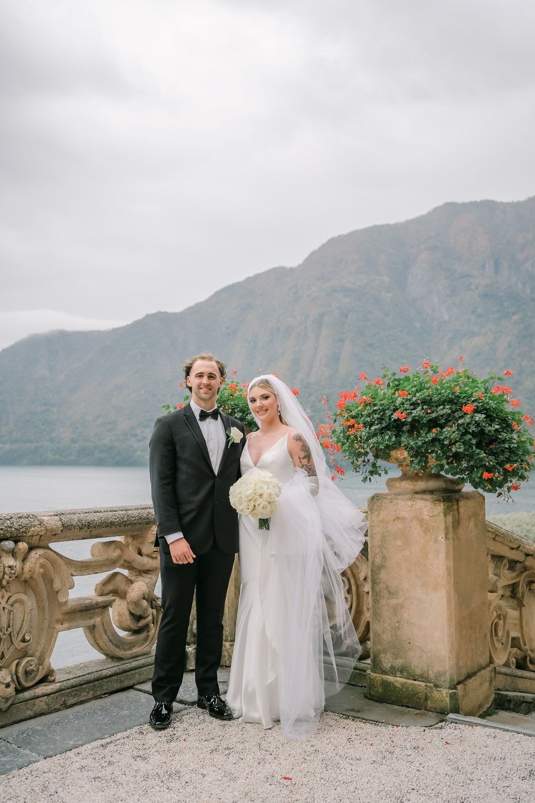 A bride and a groom standing lakeside with a great view of a mountain during their small wedding in Italy