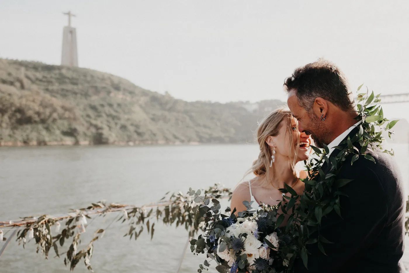 Bride holding a bouquet with her groom, and the Tagus river and Portuguese hills in the background